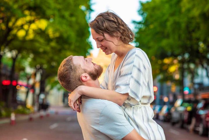 A man is carrying a woman in his arms on a city street.