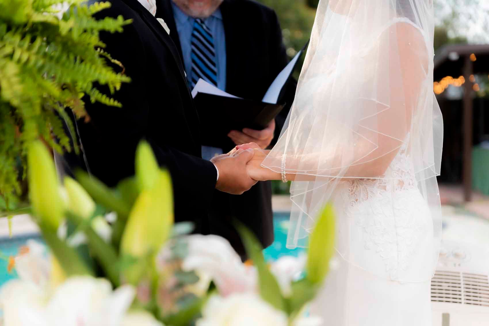 A bride and groom are holding hands during their wedding ceremony.