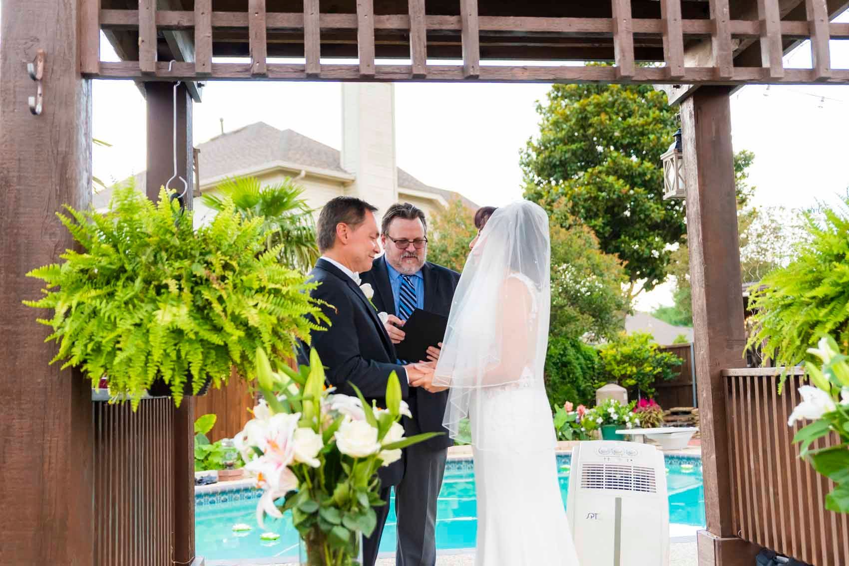 A bride and groom are holding hands during their wedding ceremony in front of a pool.