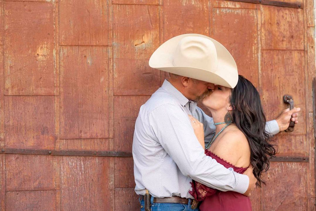 A man in a cowboy hat is kissing a woman in front of a rusty door.