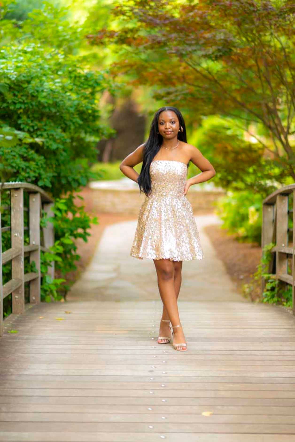 A woman in a gold dress is standing on a wooden bridge.