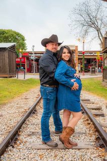 A man and a pregnant woman are standing on train tracks.