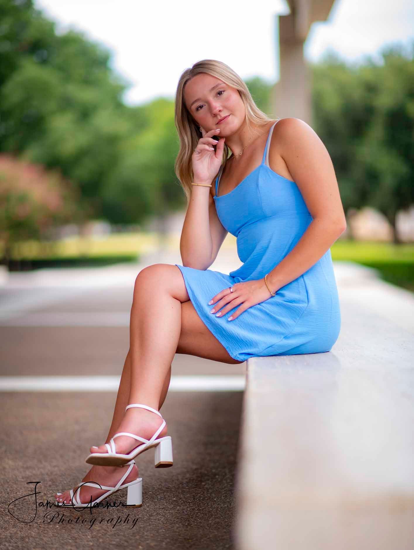 A woman in a blue dress and white heels is sitting on a bench.