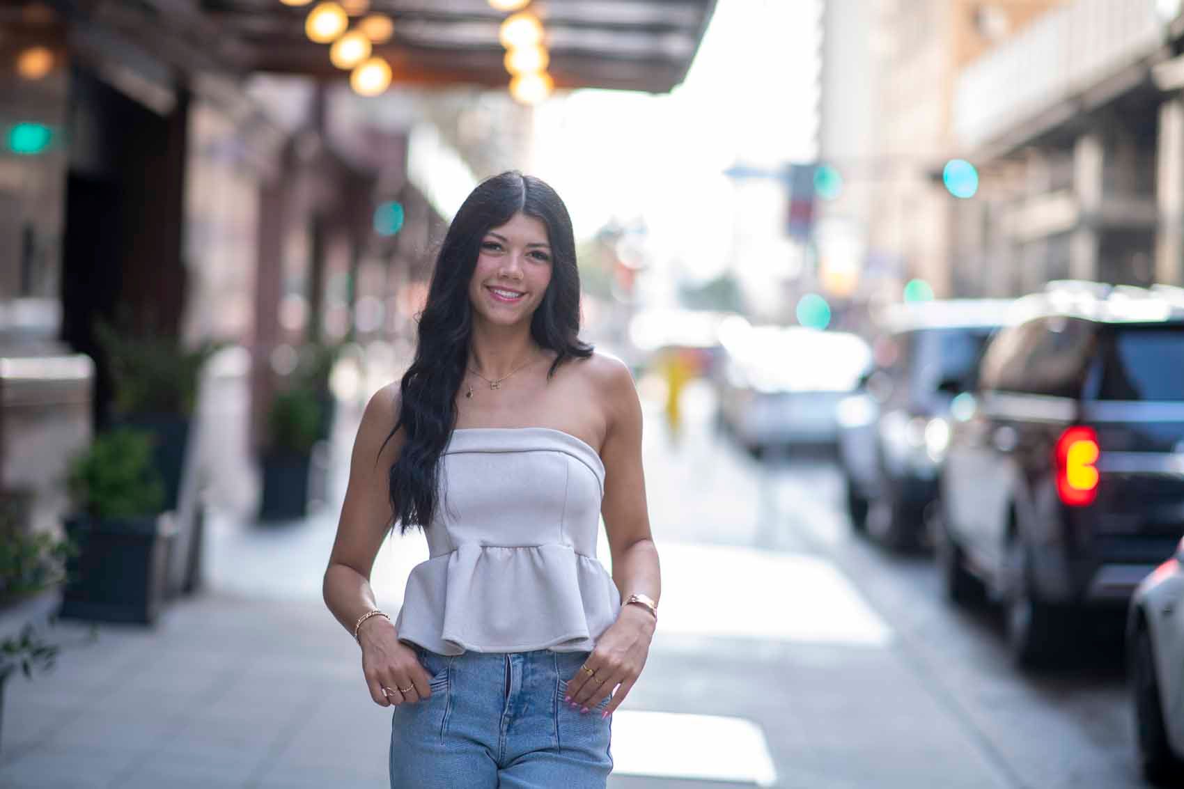 A woman is walking down a city street wearing a strapless top and jeans.