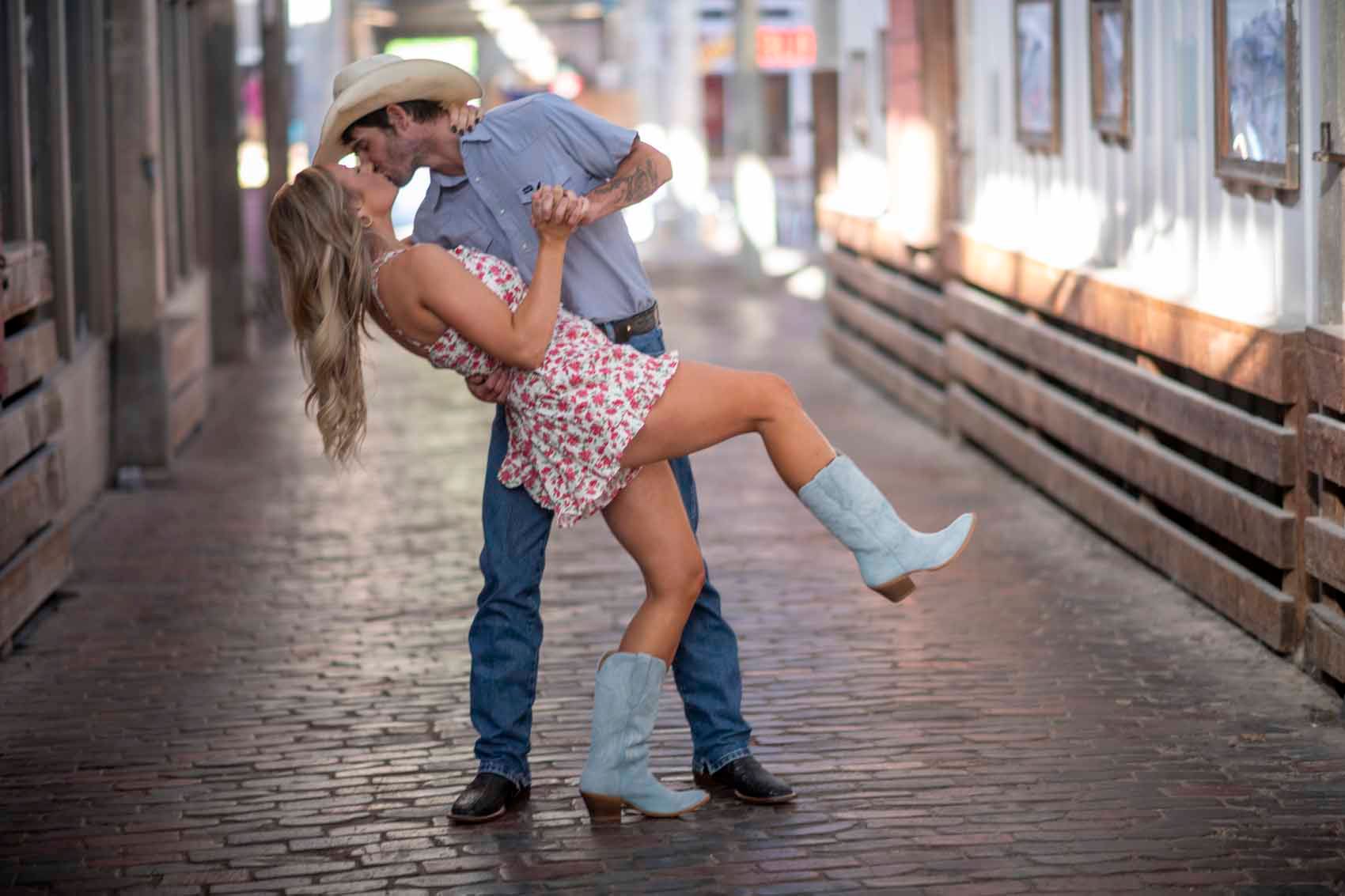 A man in a cowboy hat is holding a woman in his arms and kissing her.