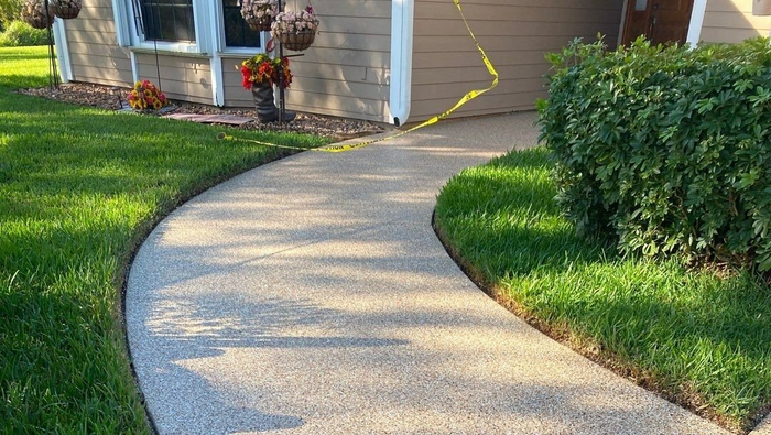 A concrete walkway leading to a house with a lush green lawn.