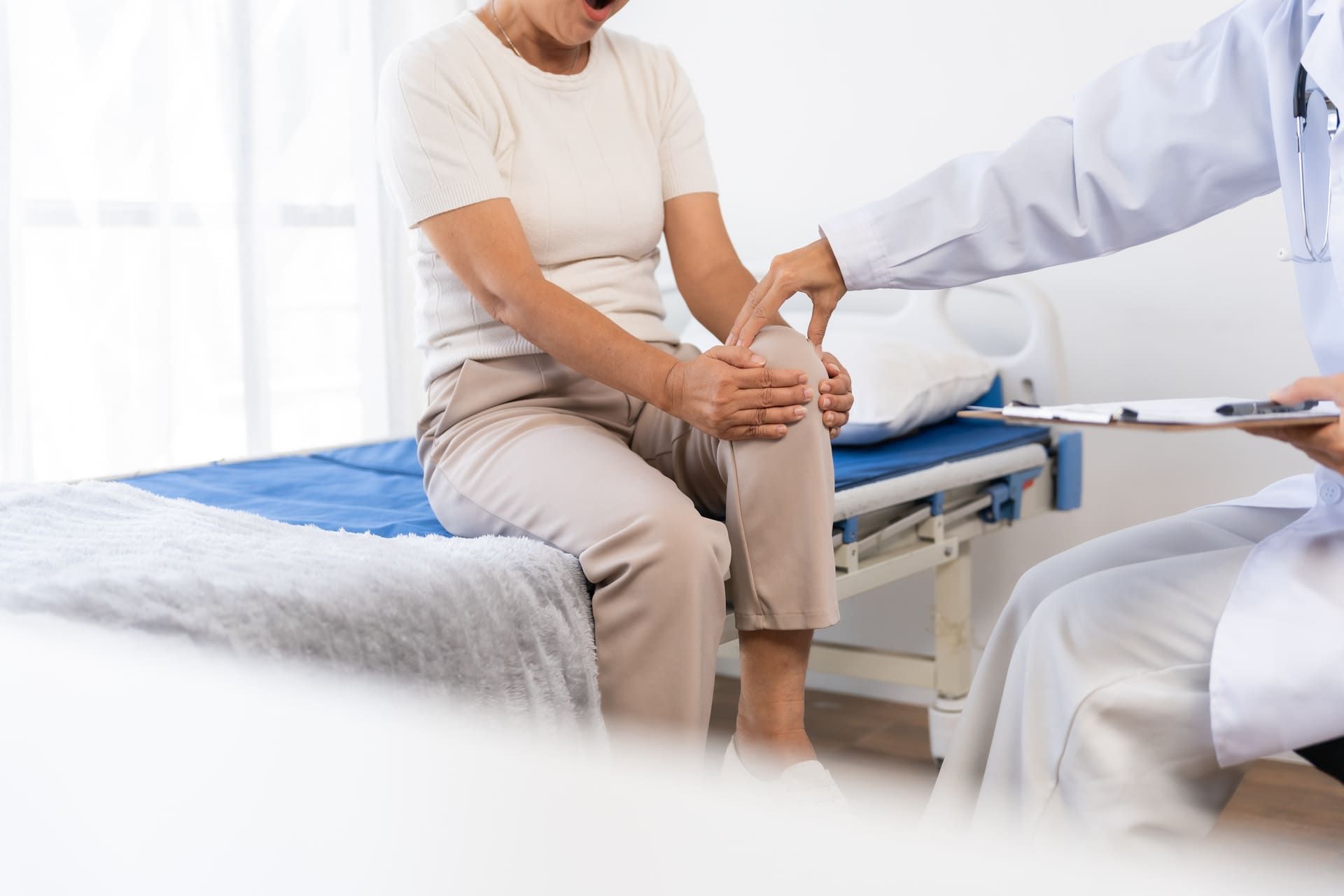 Doctor examining a senior woman's knee to diagnose joint pain. Healthcare professional providing care for an elderly patient