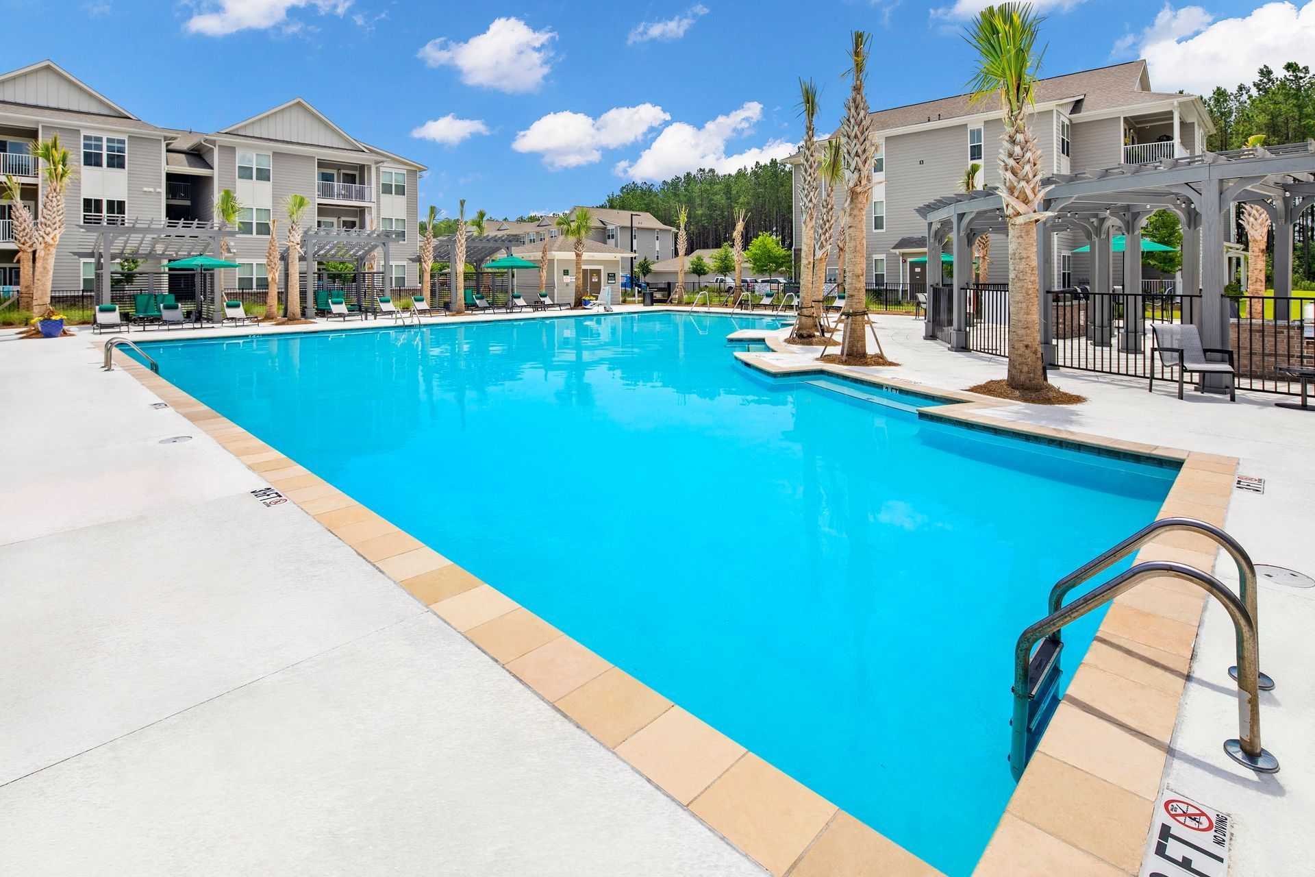 Large outdoor pool with turquoise water surrounded by buildings, palm trees, and a sunny sky.