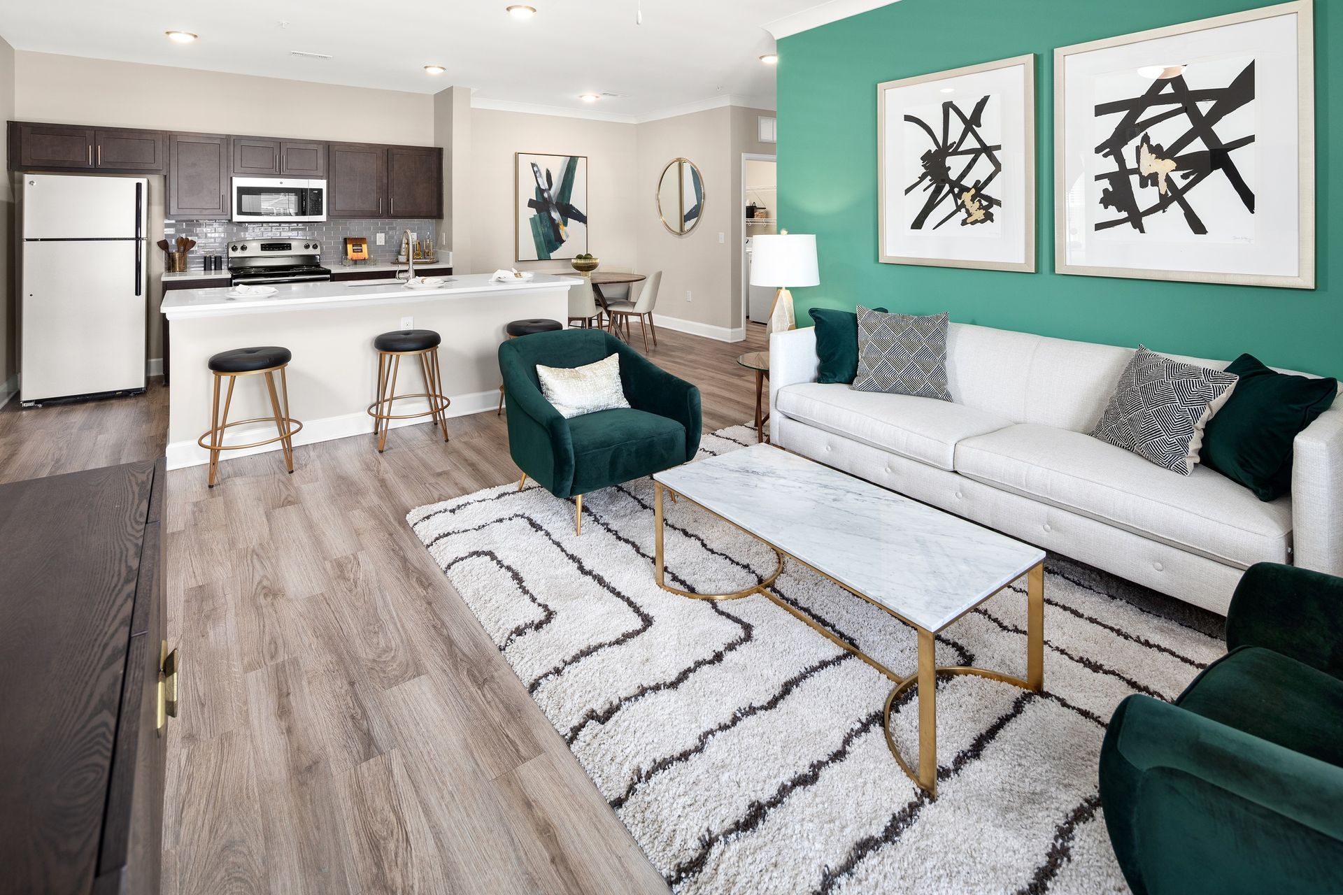 Open-concept apartment: kitchen with stainless steel appliances, living area with green accent wall and white couch.