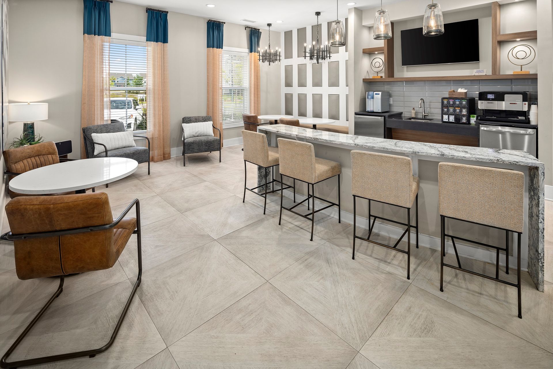 Lounge area with bar, seating, coffee machine, and TV in a modern space with large windows and light-colored tile floor.