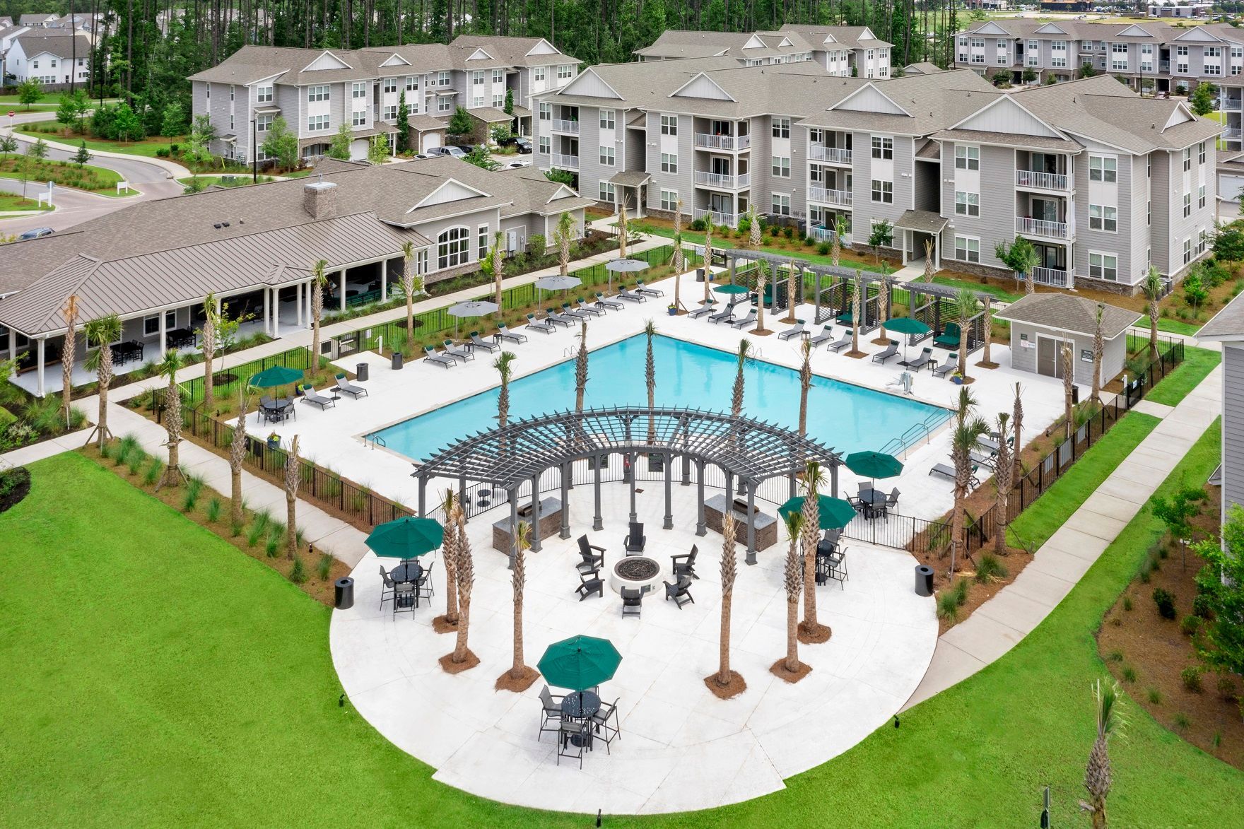 Aerial view of an apartment complex with a pool, lounge area, and surrounding buildings.