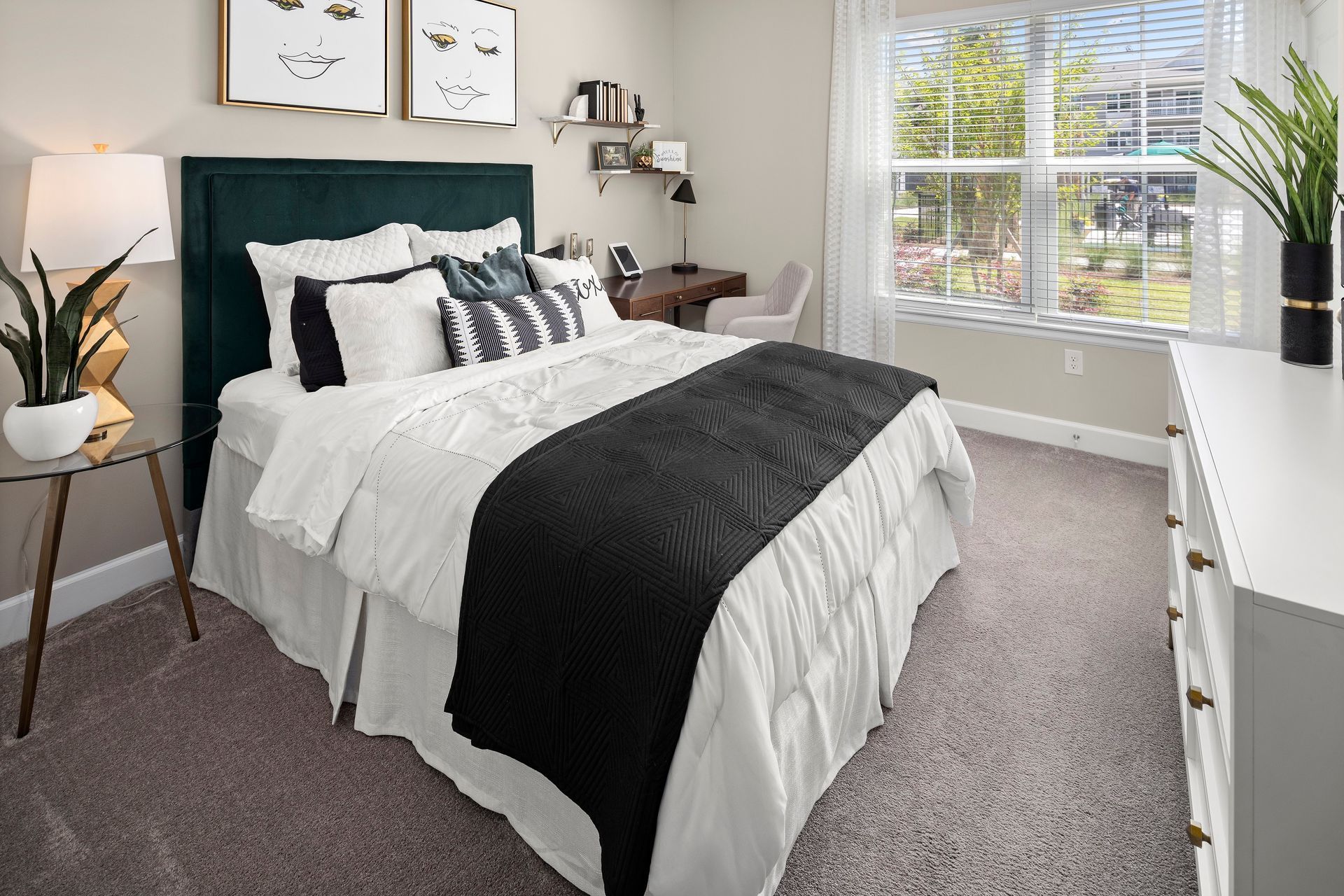 Bedroom with green headboard, white bedding, black blanket, desk, art, and a window.