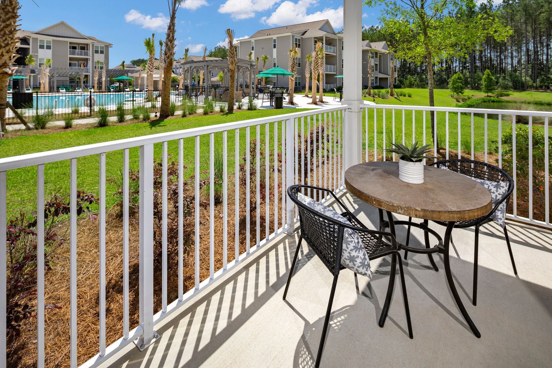 Balcony with a small table and chairs, overlooking a pool and apartment buildings.