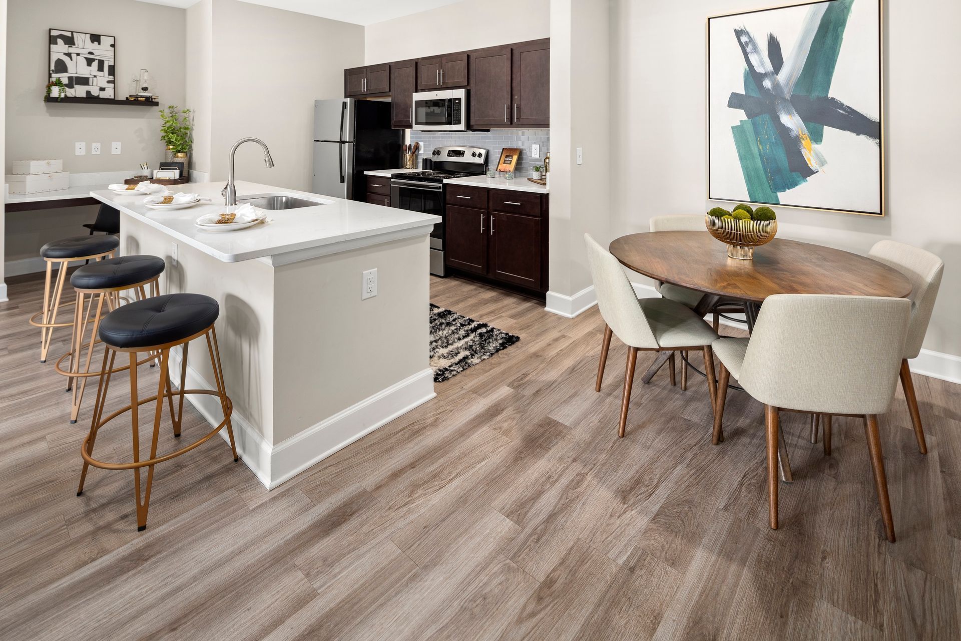 Modern kitchen and dining area with island, stools, round table, and artwork.