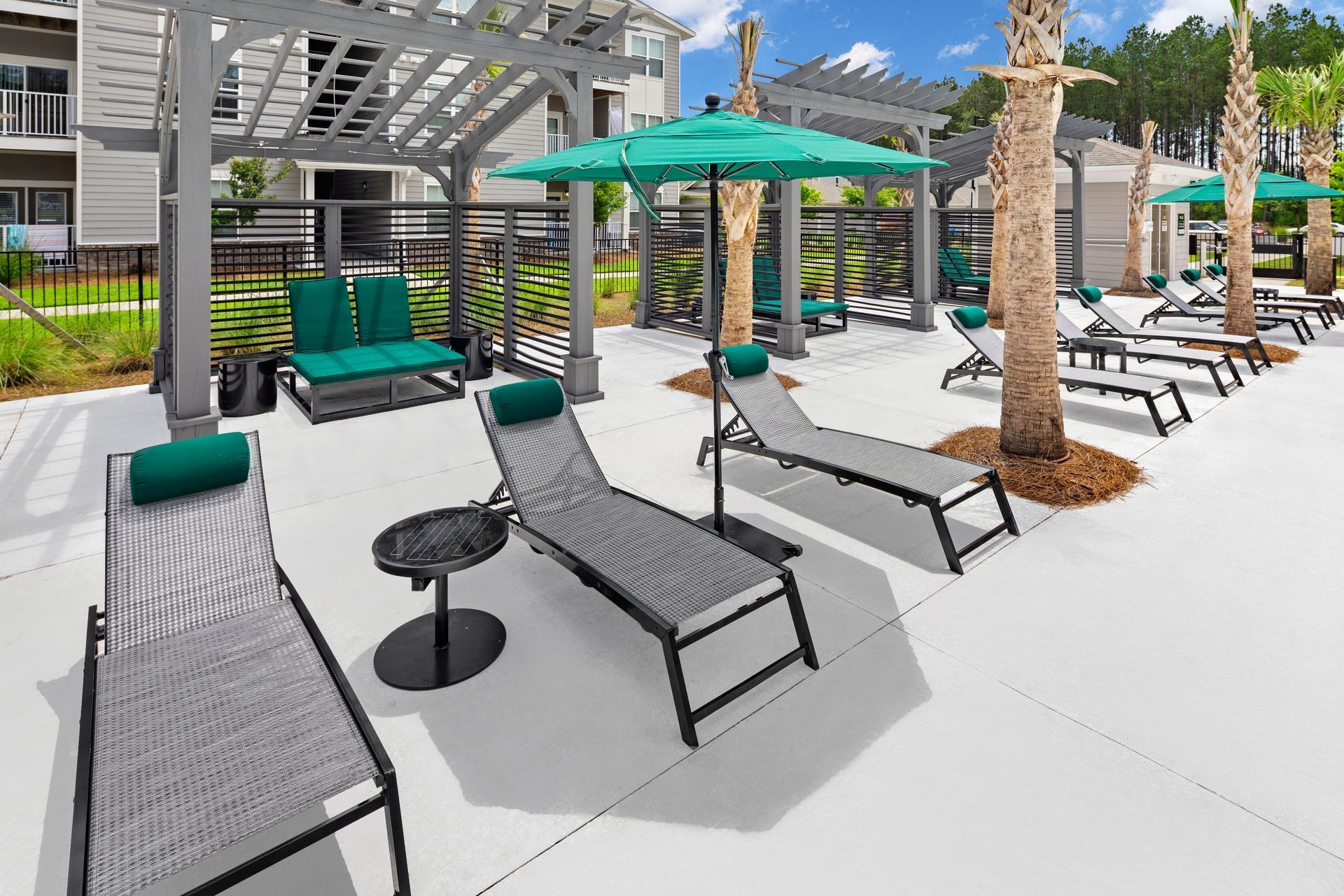 Poolside lounge area with gray lounge chairs, teal umbrellas, and palm trees.