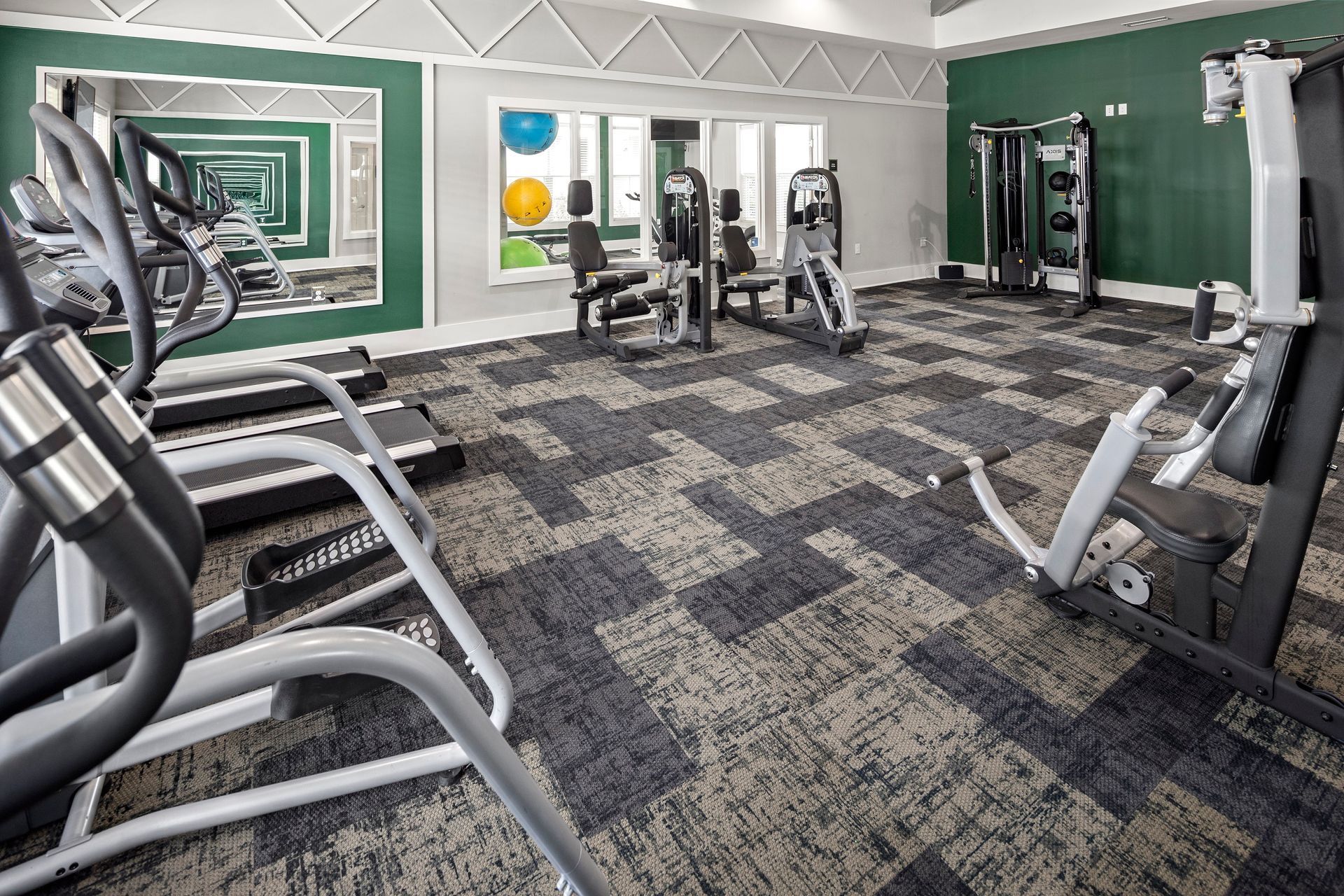 Gym with exercise equipment: treadmills, weight machines, and a patterned carpet floor.