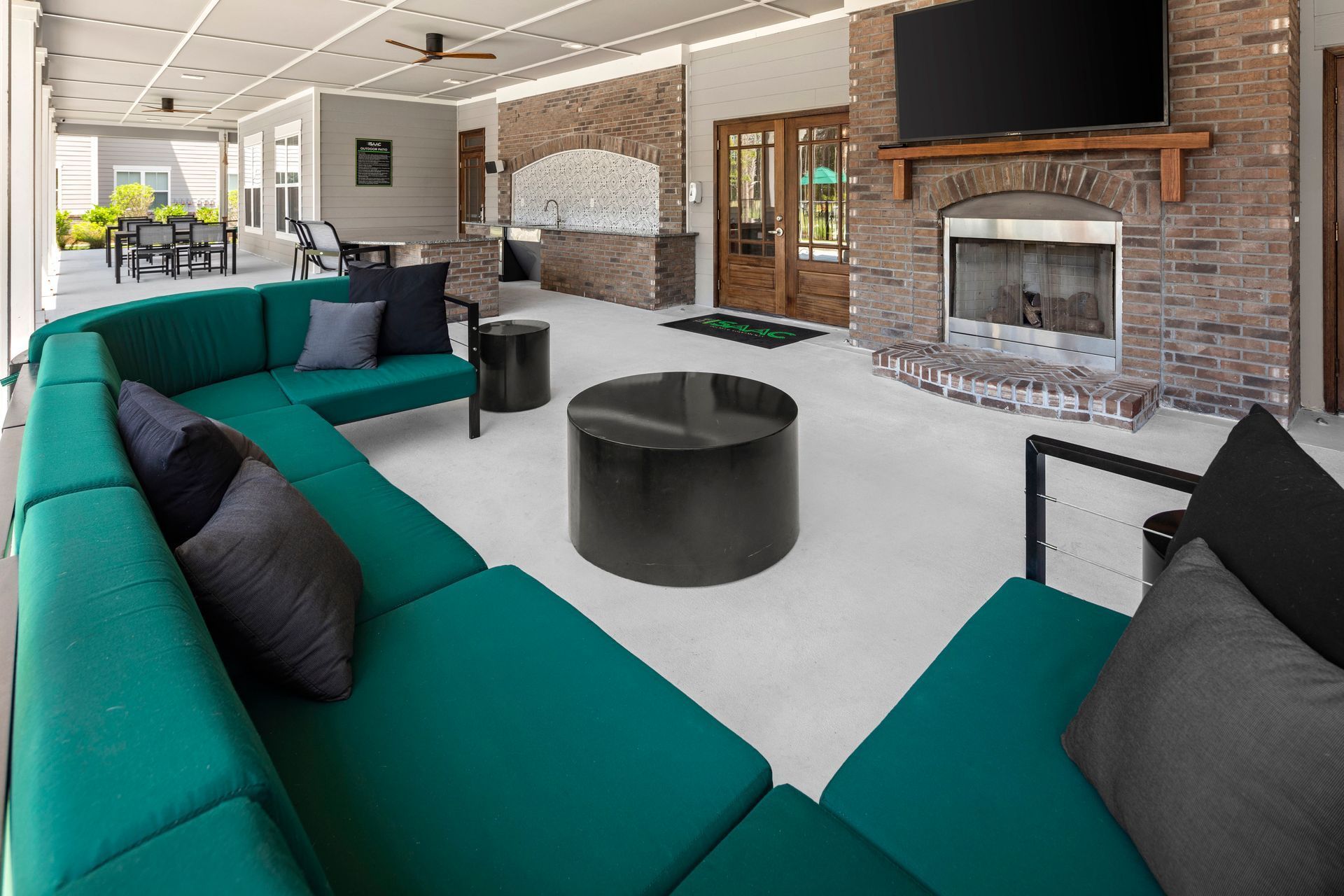Teal sectional sofa on a patio with fireplace and TV. Black tables and gray pillows.