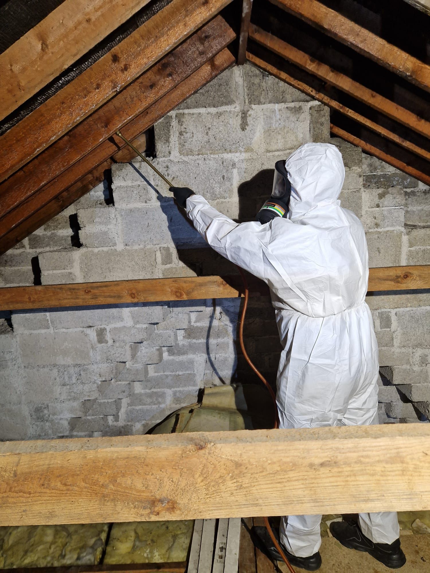 A man in a protective suit is spraying a brick wall with a sprayer.