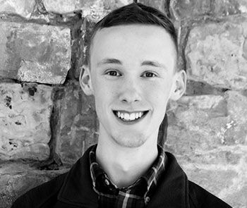 Smiling person in a dark jacket standing before a stone wall backdrop