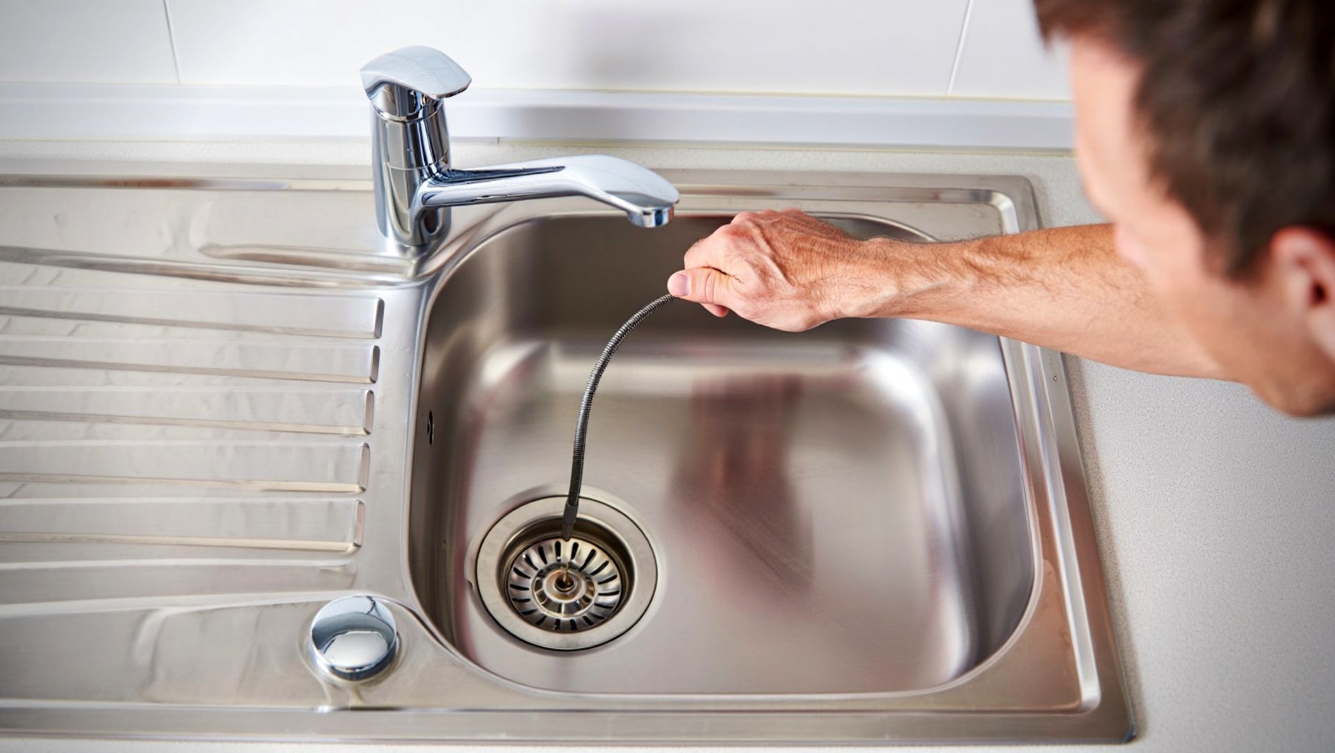 Hand turning a faucet over a stainless steel kitchen sink with a drain visible