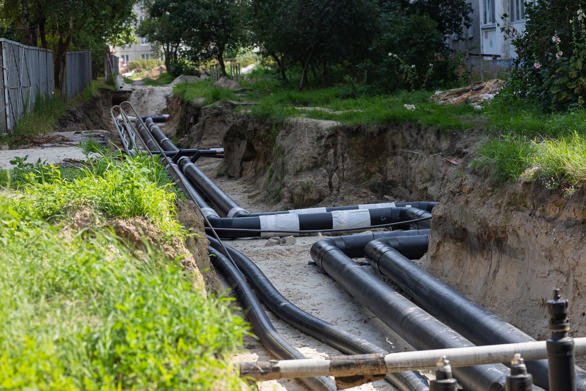 Black utility pipes laid in a dug trench beside a grassy roadside and trees