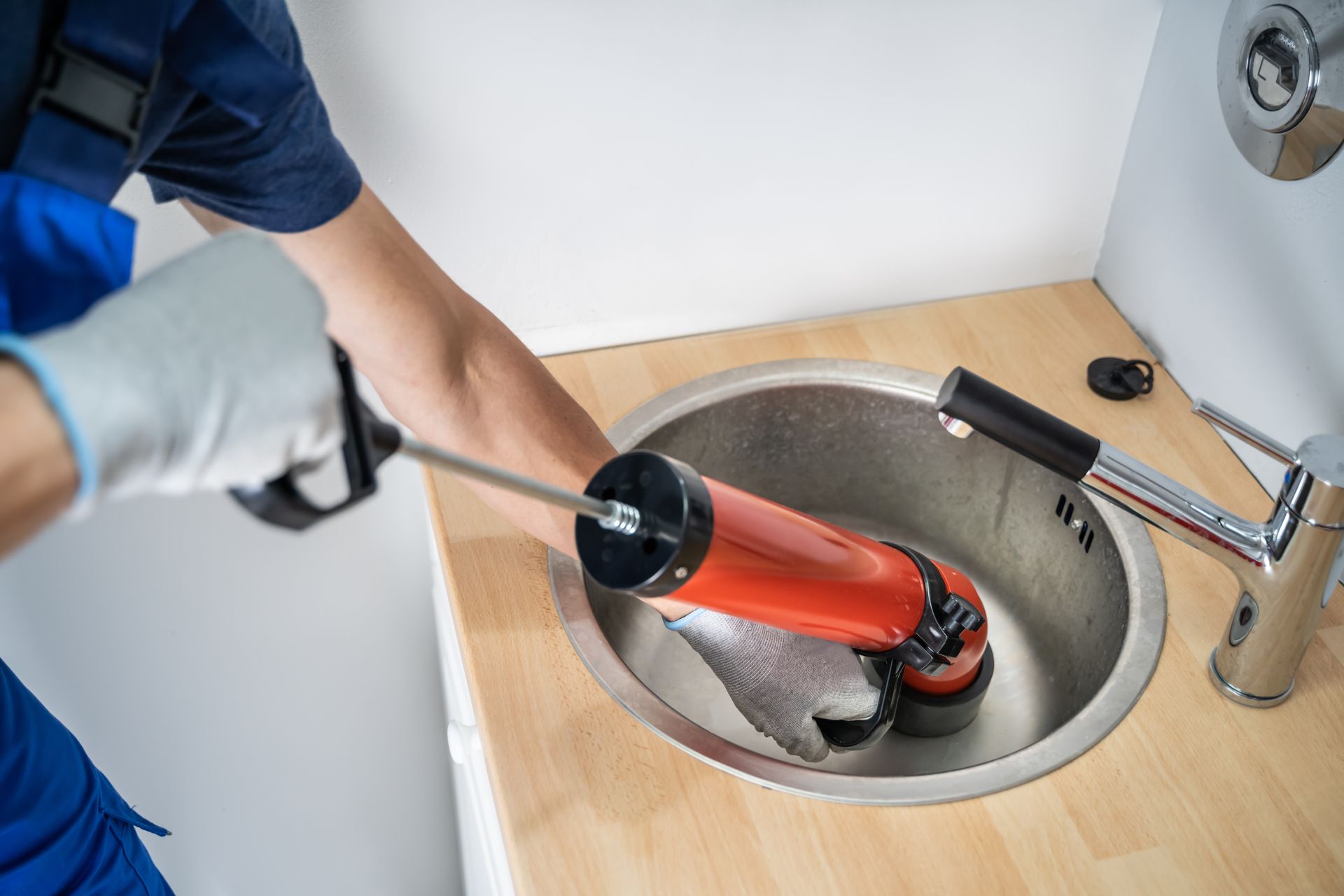 Plumber using a drain snake to clear a sink clog in a bathroom.