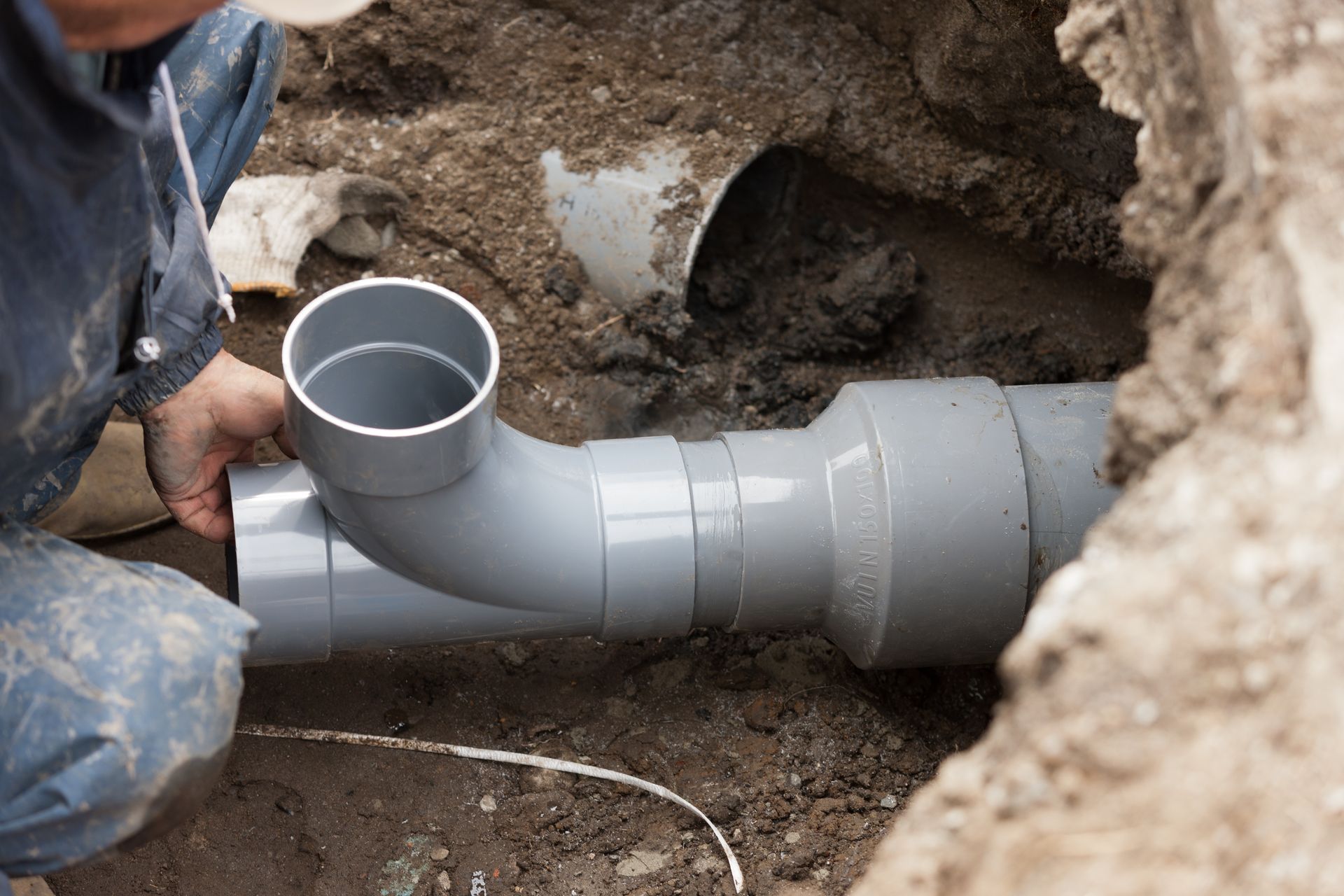 Worker installing gray PVC pipe in a trench underground