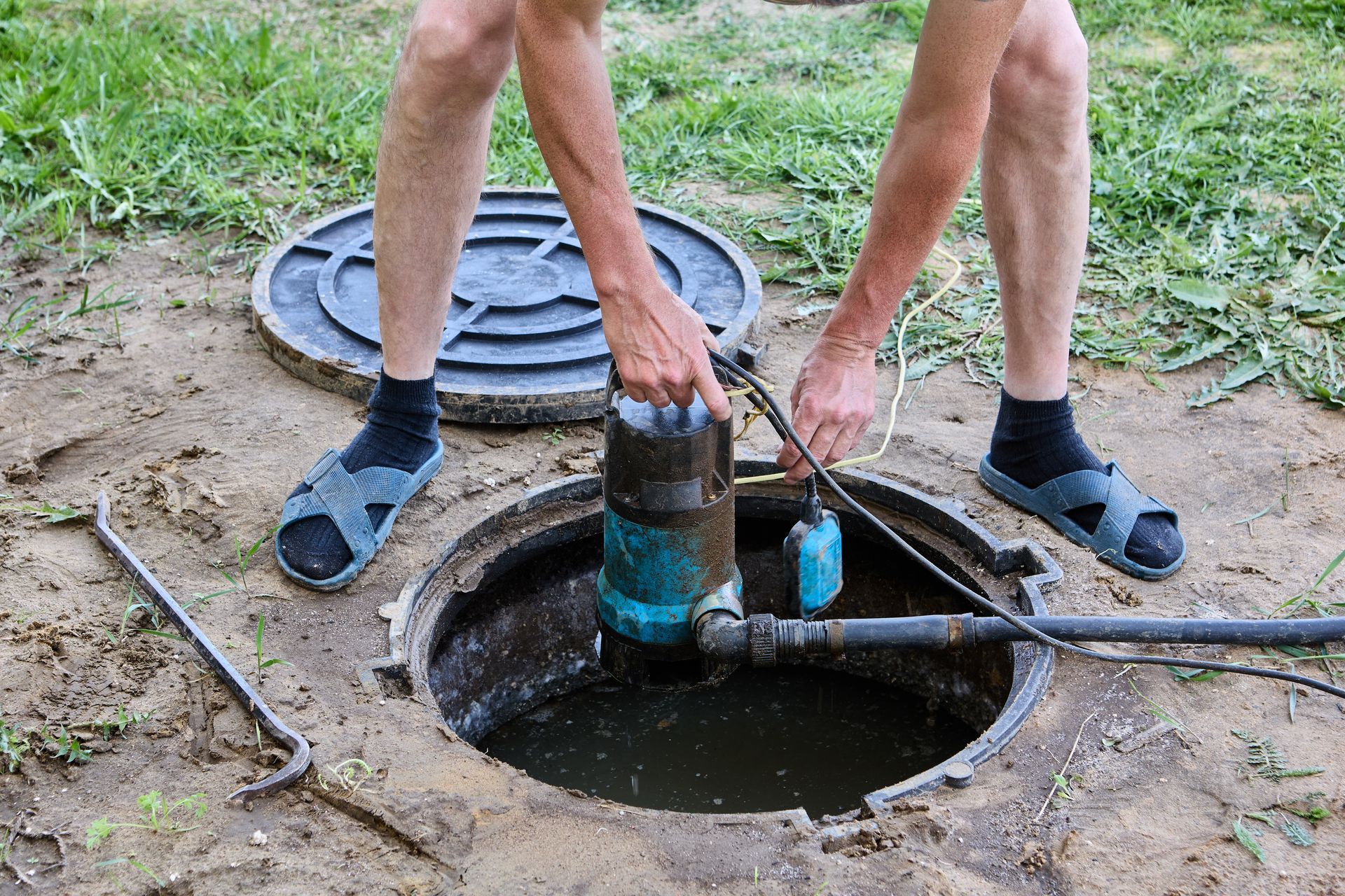 Person working on a water well, lowering a submersible pump into an open manhole.