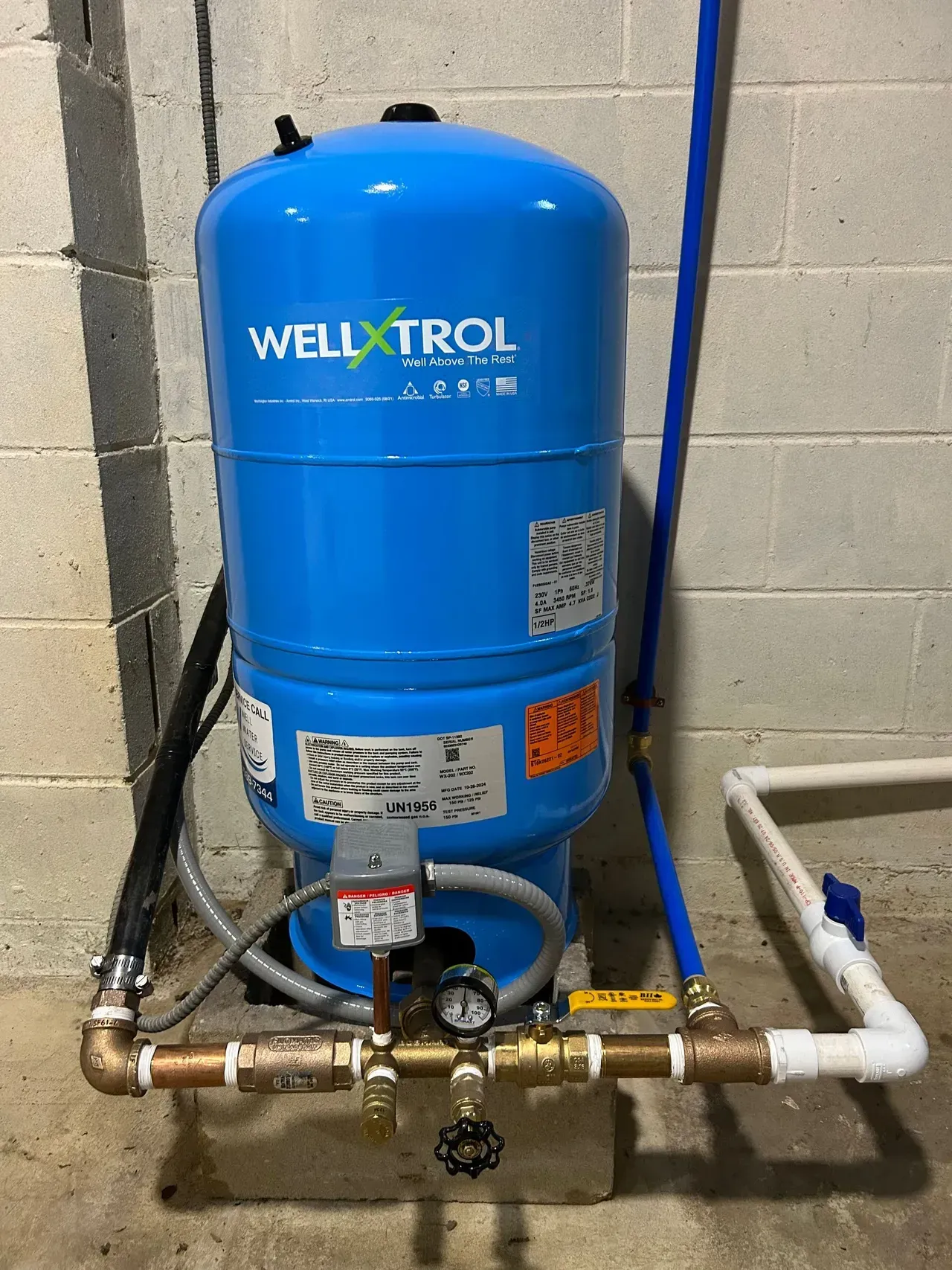 Blue WELLTROL pressure tank with pipes and valves in a utility room against a cinderblock wall