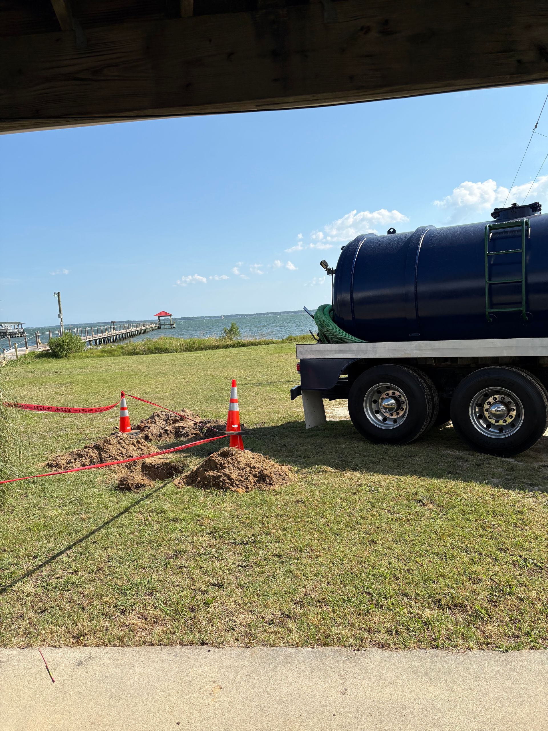 Blue tanker trailer parked on grass near orange cones and red caution tape under a clear sky