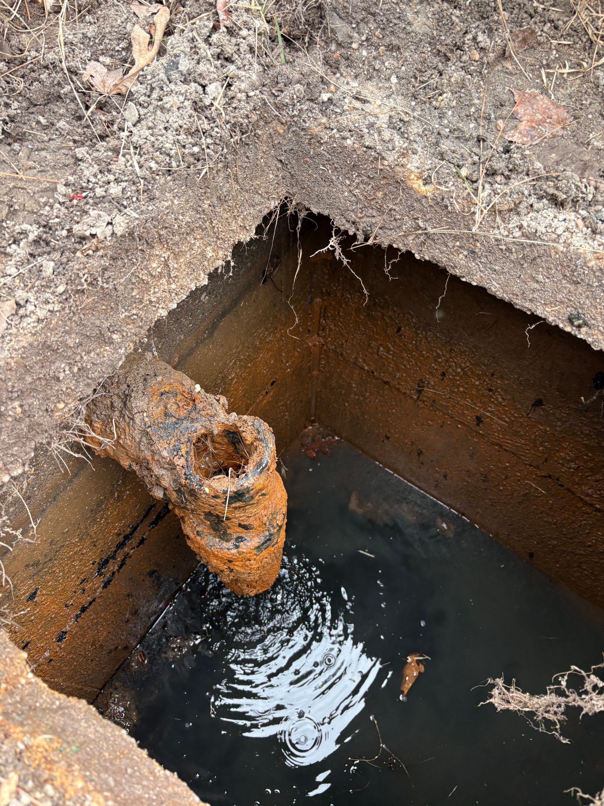 Rusty pipe protruding into a water-filled concrete pit with ripples on the surface