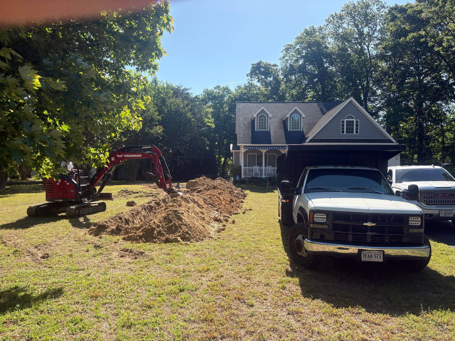 Front yard with red excavator, dirt pile, and two pickup trucks in front of a house