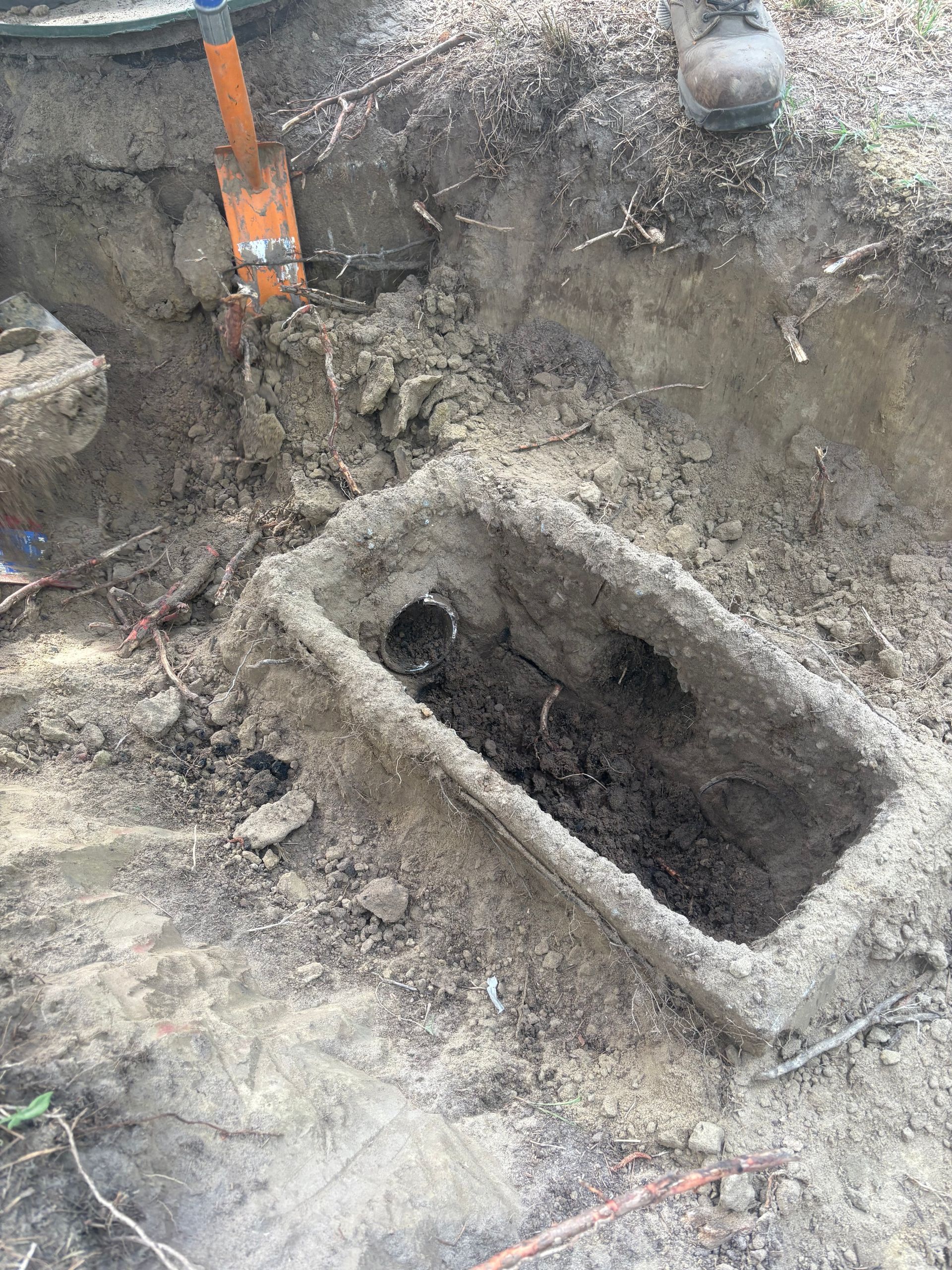 Excavator arm digging a muddy rectangular trench in a construction site