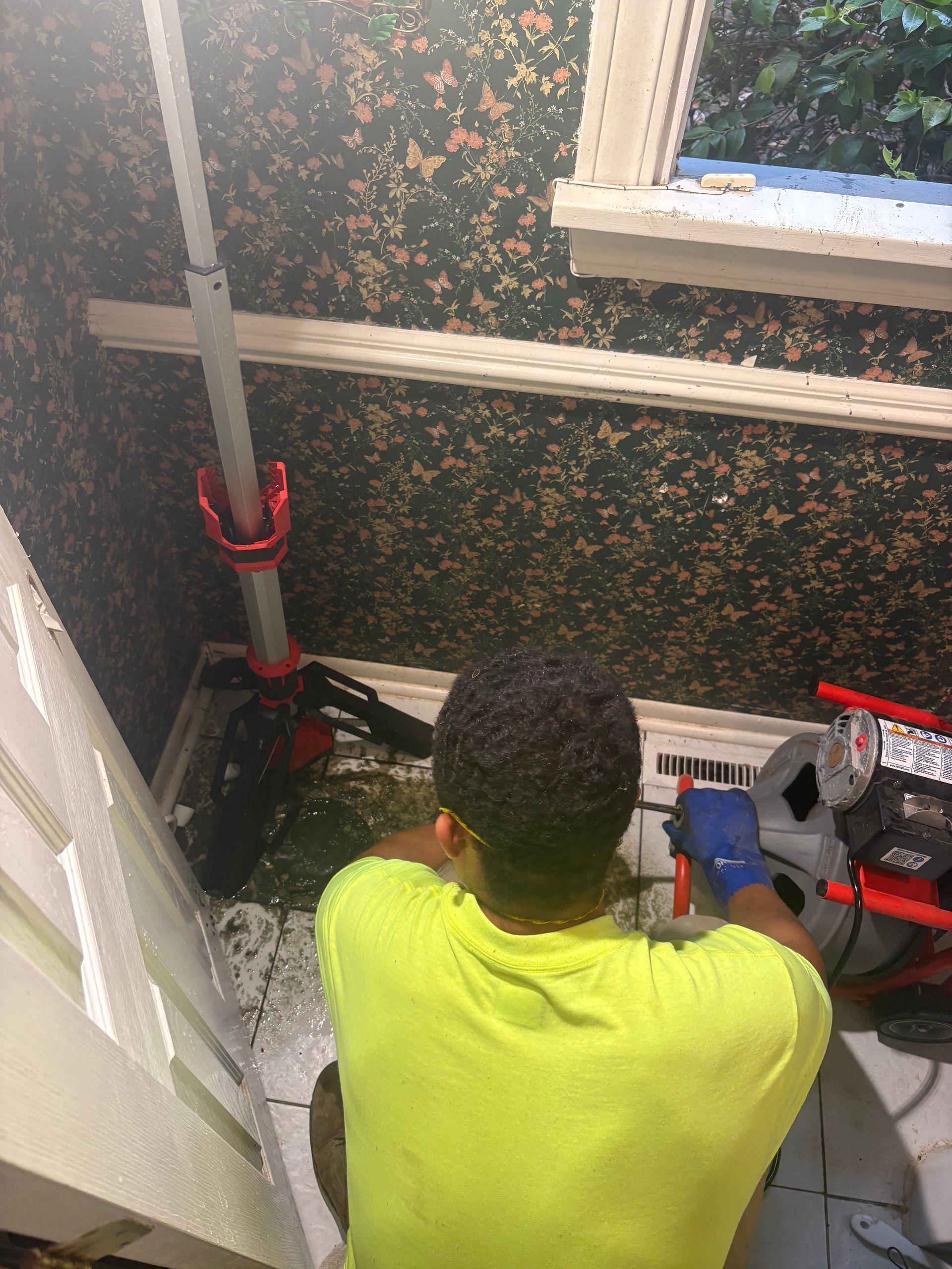 Person kneeling in a small room, working with tools near a wall and window.