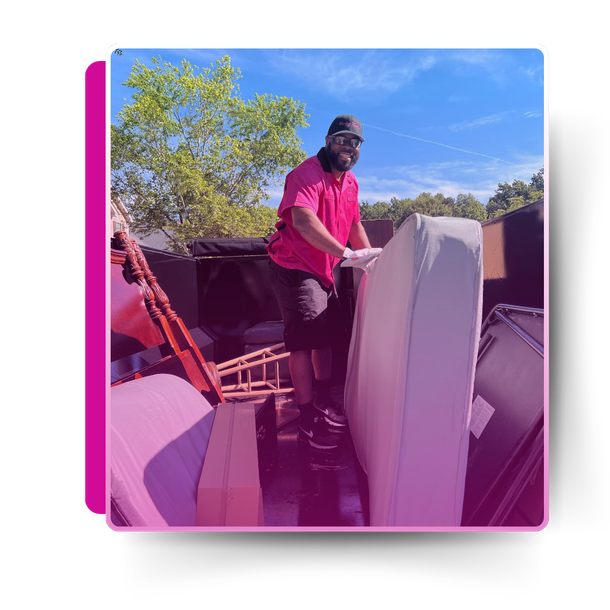 A man in the trailer truck holding a discarded mattress.