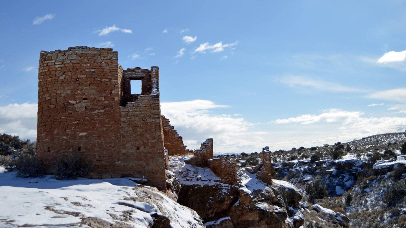 Ruined stone tower on snow-covered cliff, blue sky in the background.