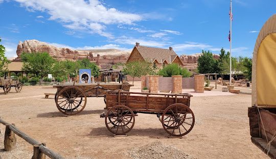 Two wooden wagons are parked in a dirt field in front of a building.