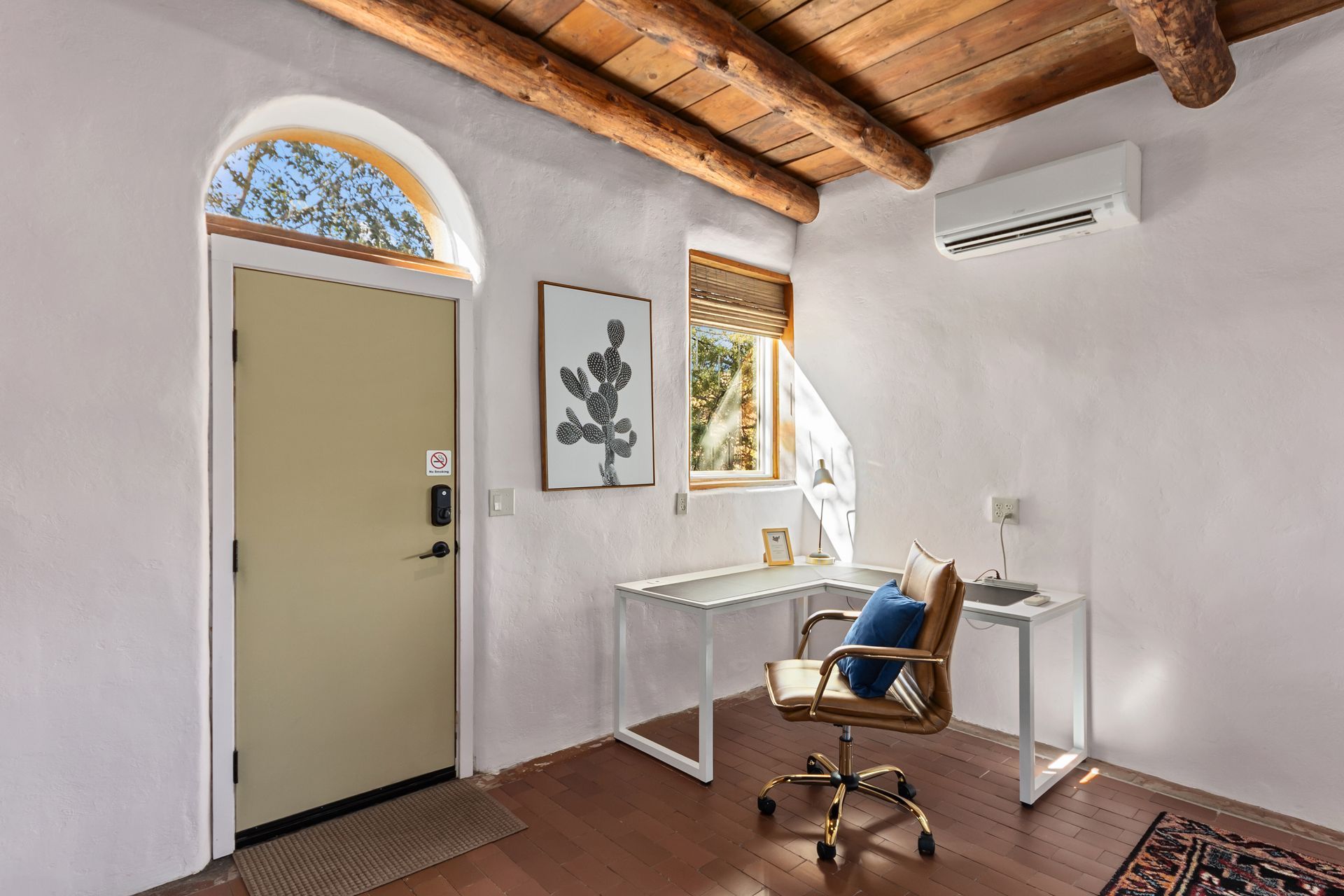 Office with white walls, desk, cactus art, arched doorway, wood beams.
