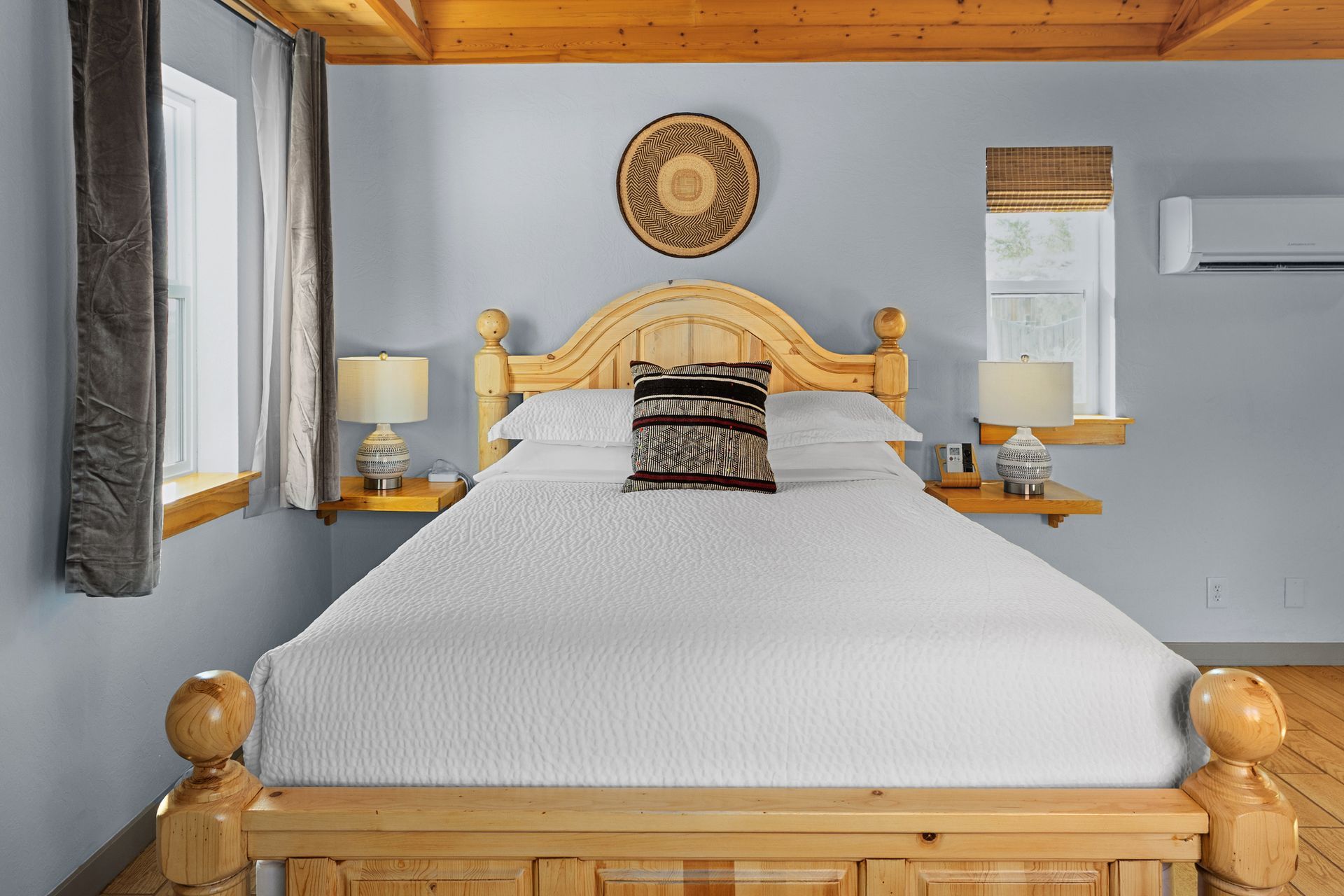 Bedroom with light blue walls, wooden bed frame, and decorative woven art.