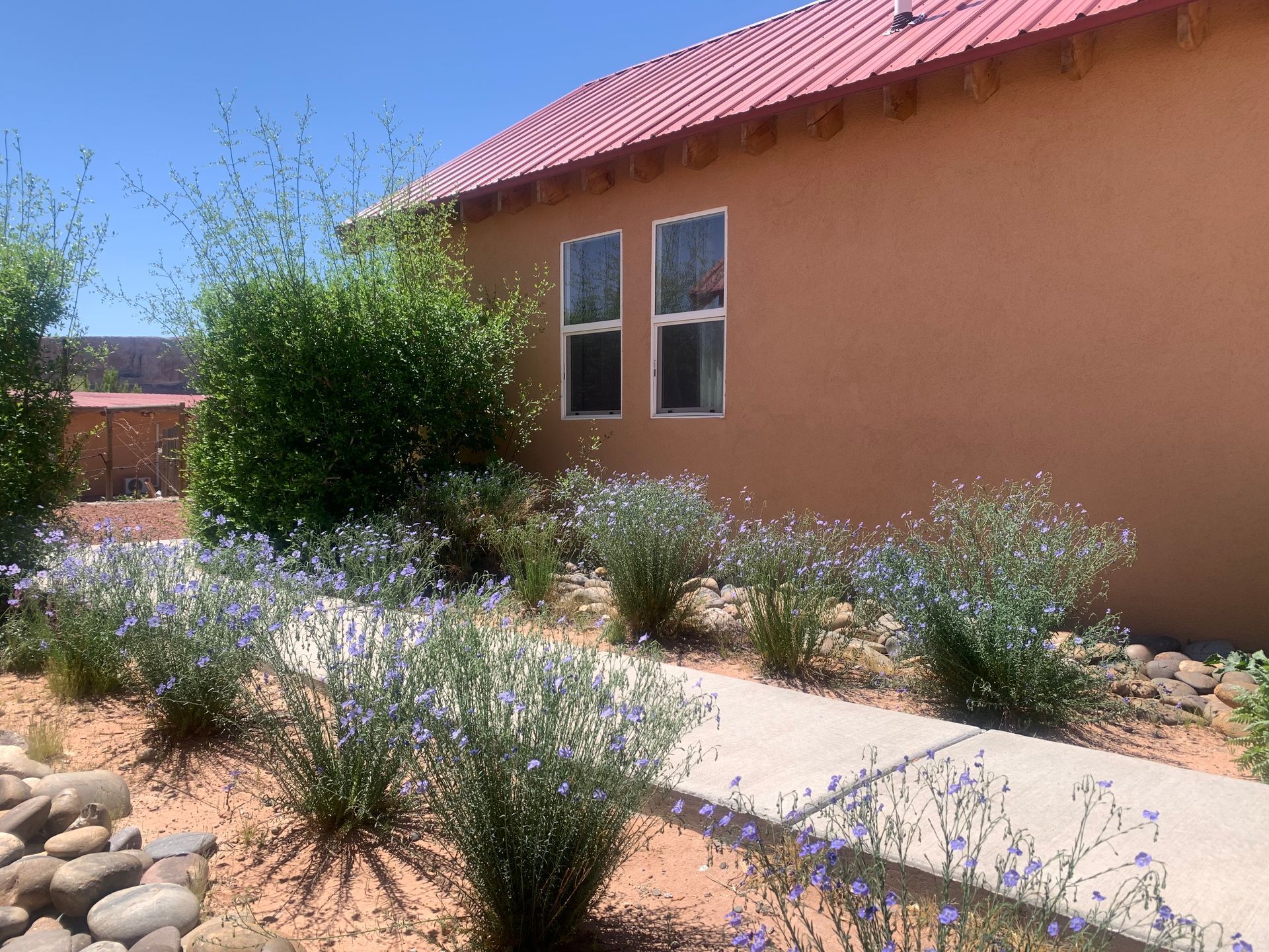 A house with a red roof is surrounded by flowers and bushes.