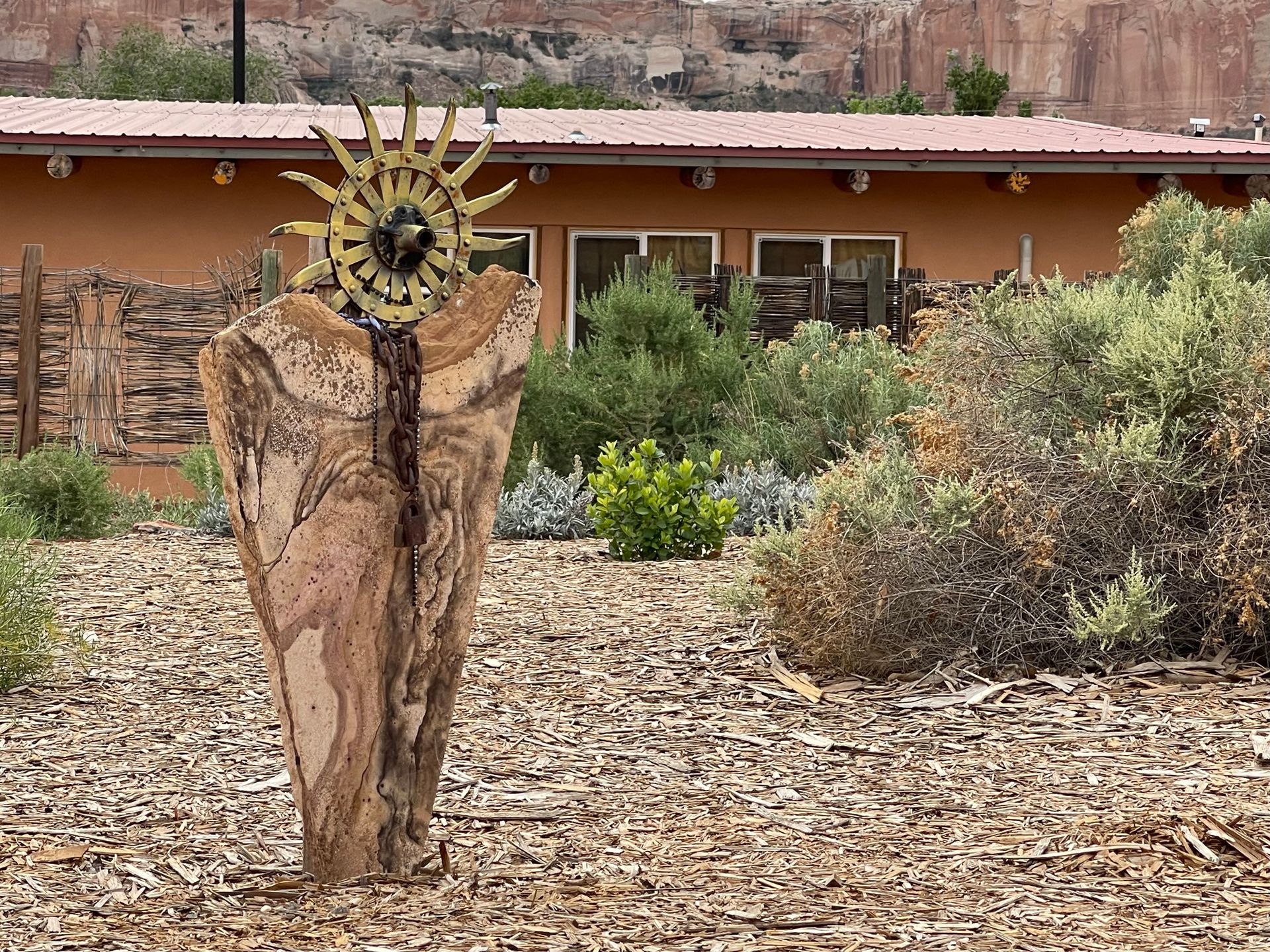 A wooden sculpture of a sun is sitting in a pile of mulch in front of a house.