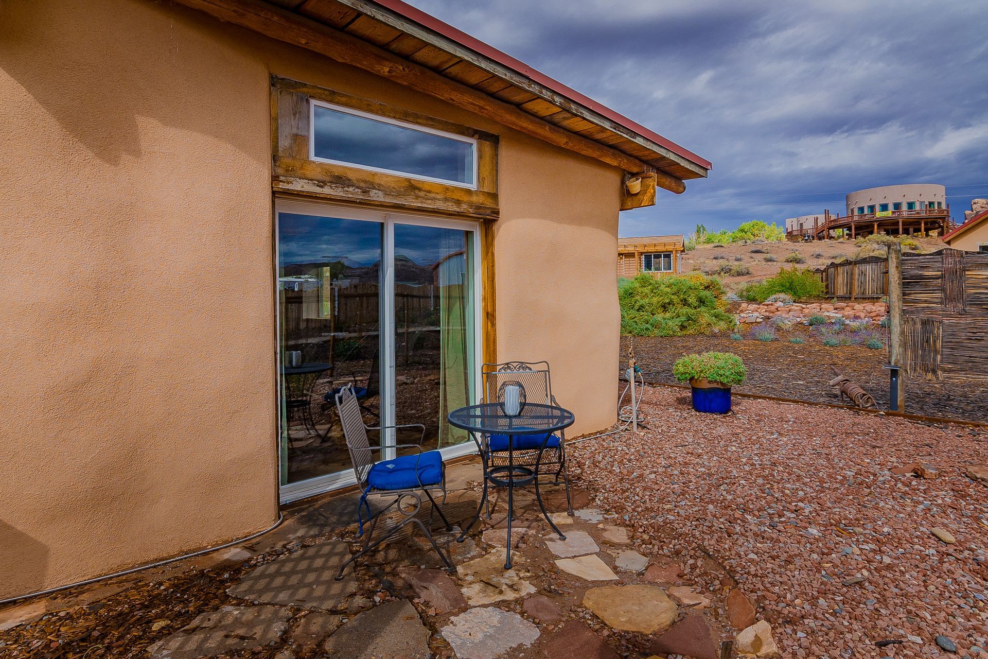 Back patio with blue chairs and a table. A sliding glass door and window are visible.