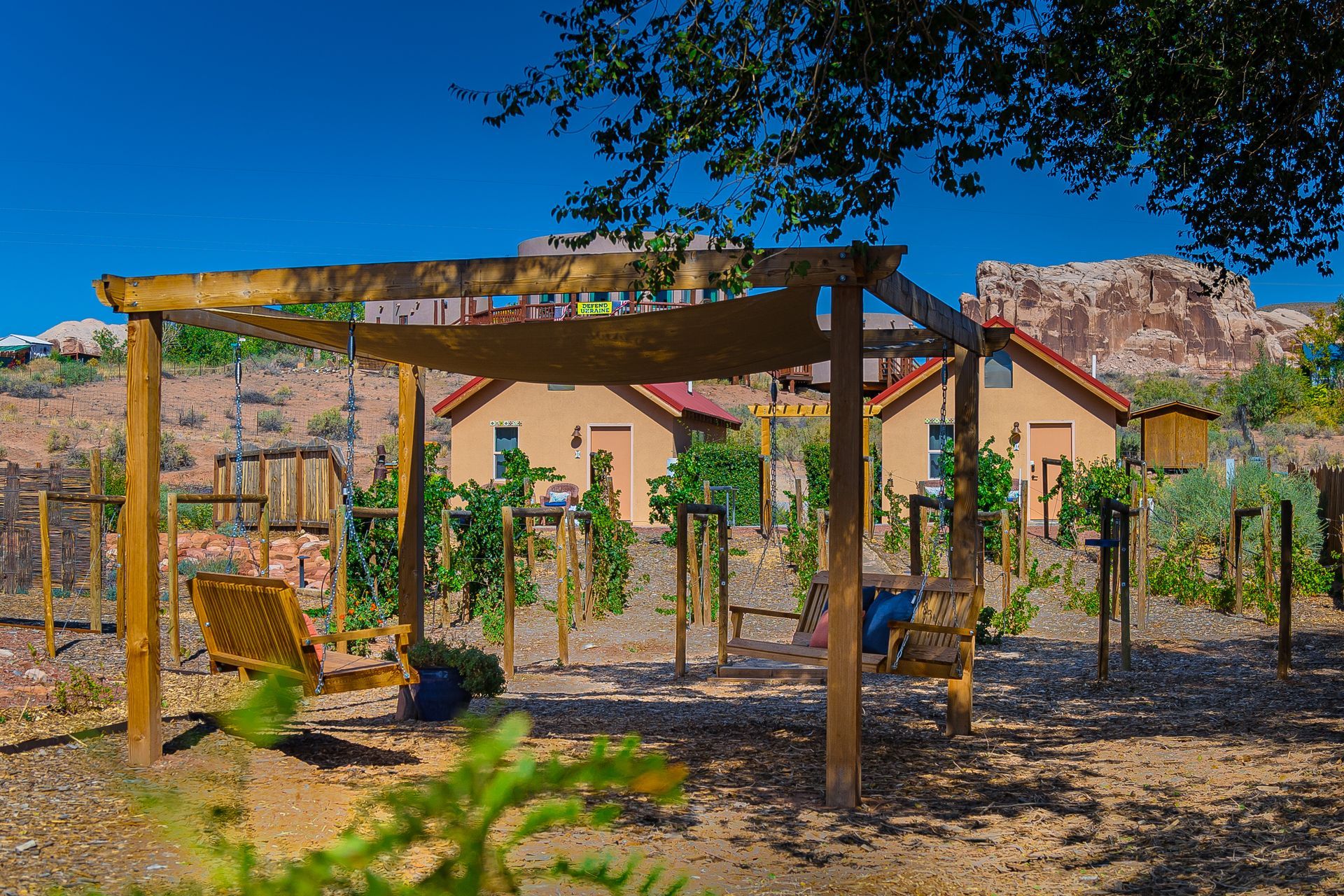 Wooden swing set and small houses with red roofs against a rocky mountain backdrop under a blue sky.