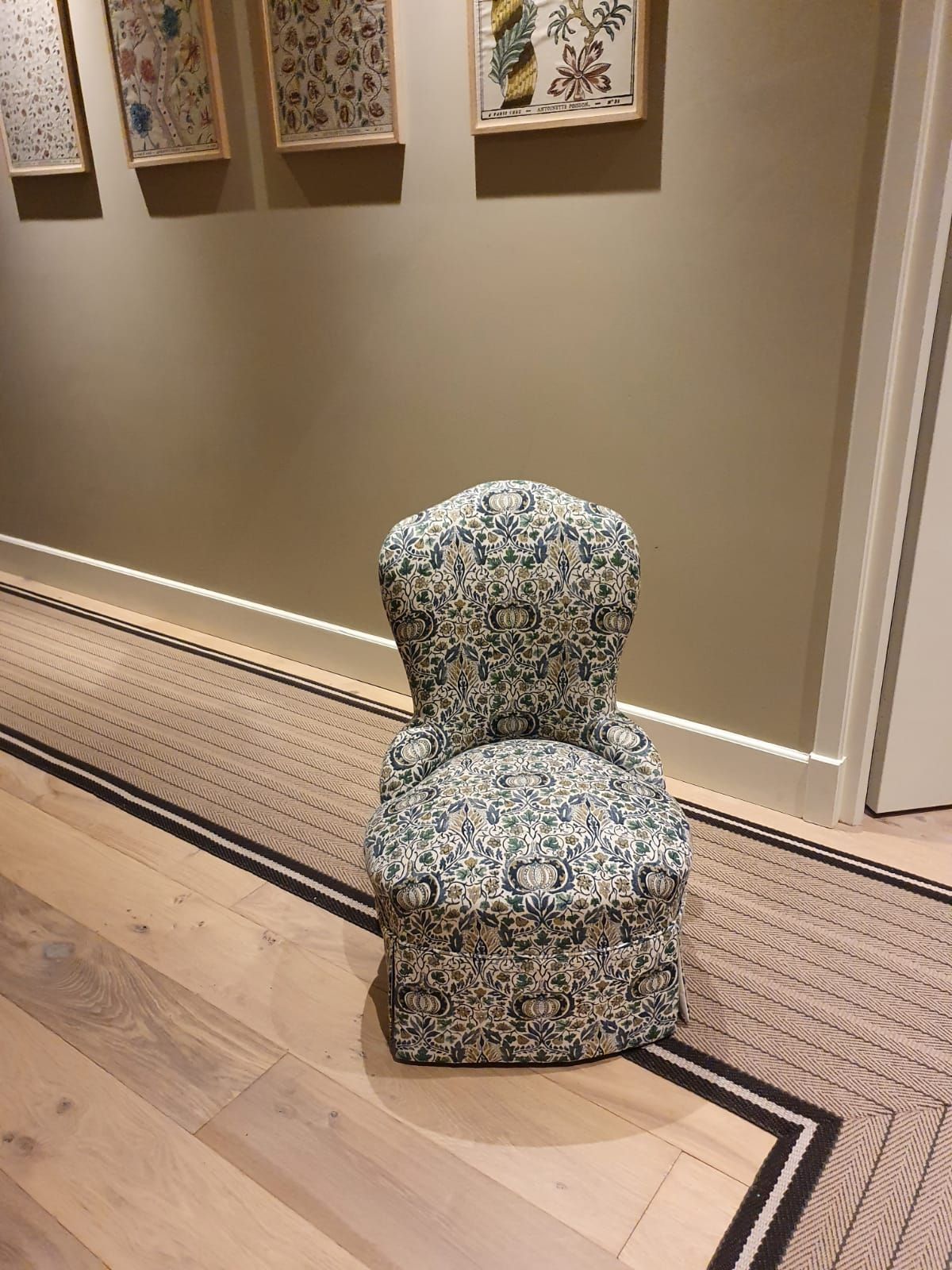 Chaise rembourrée à motif floral dans le couloir, avec œuvre d'art encadrée. Parquet en bois clair avec bordure à motifs.