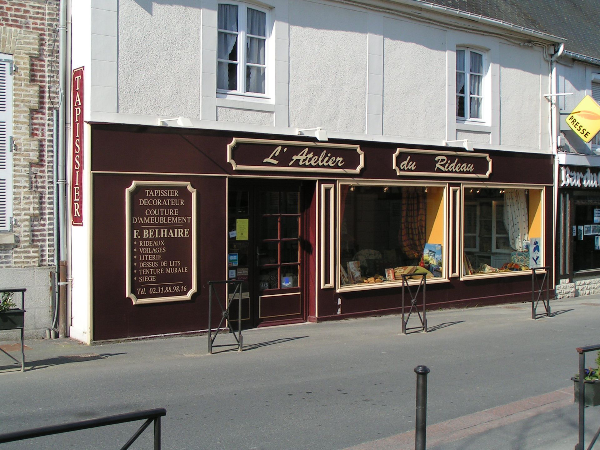 Devanture marron avec l'inscription « L'Atelier du Tableau ». Murs blancs, boiseries marron et petite enseigne sur le côté.