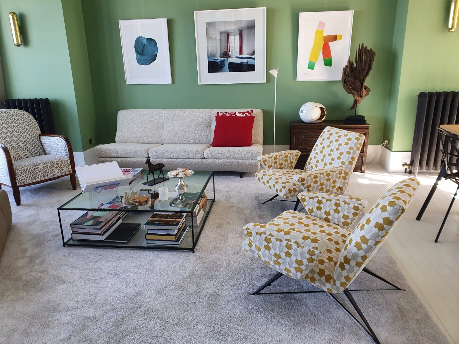 Un salon avec des murs verts, un canapé blanc, deux fauteuils à motifs et de l'art abstrait au-dessus du canapé.