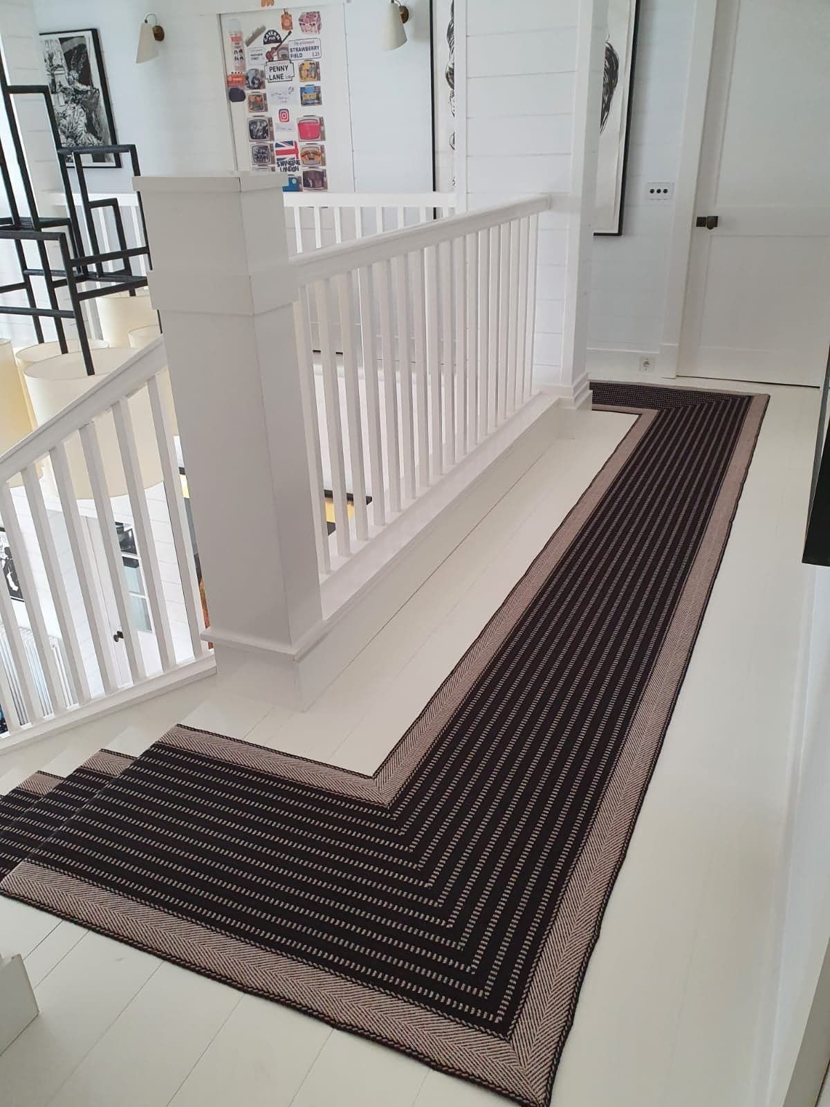 Un long tapis rayé marron et beige borde un couloir et un escalier blancs.