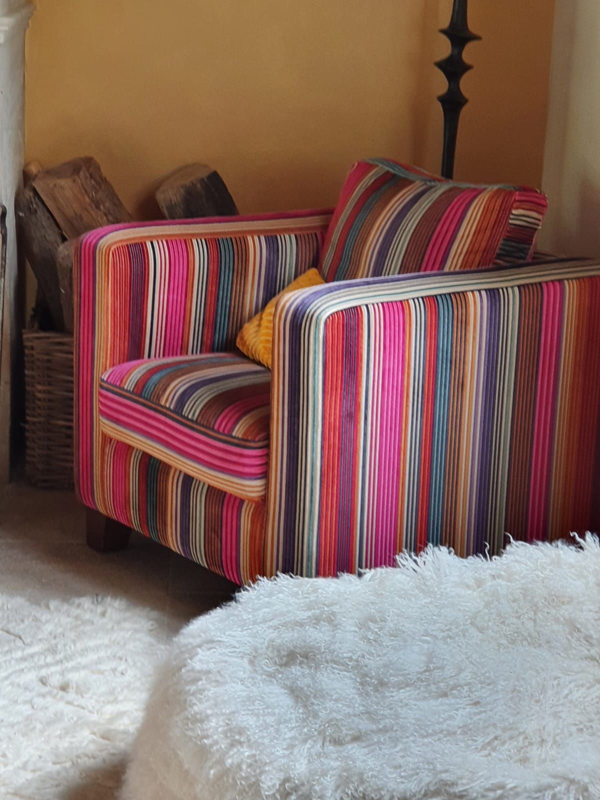 Fauteuil à rayures colorées avec coussins sur un tapis blanc moelleux dans une pièce avec un mur doré.