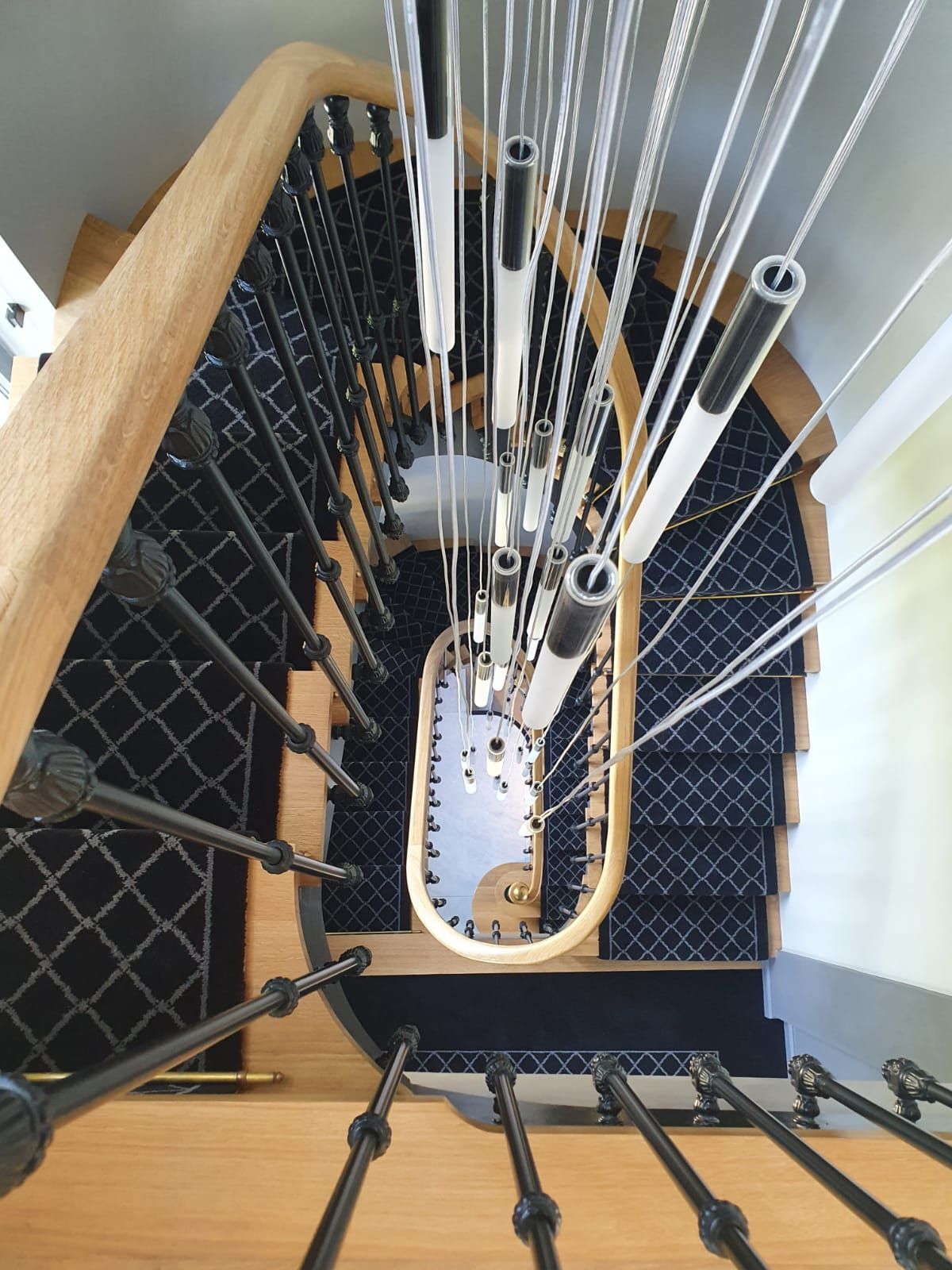 Vue de haut en bas d'un escalier en colimaçon avec moquette noire, rampe en bois et rampe à câbles moderne.