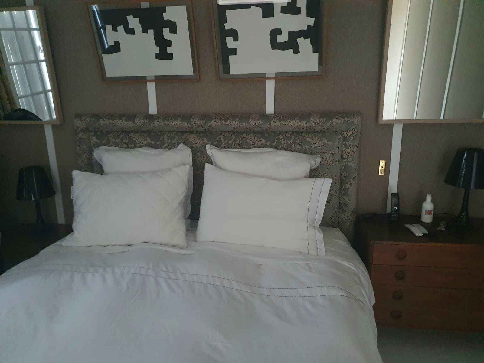 Un lit double avec draps et oreillers blancs, flanqué de tables de chevet avec lampes. Deux œuvres d'art abstraites en noir et blanc sont suspendues au-dessus.